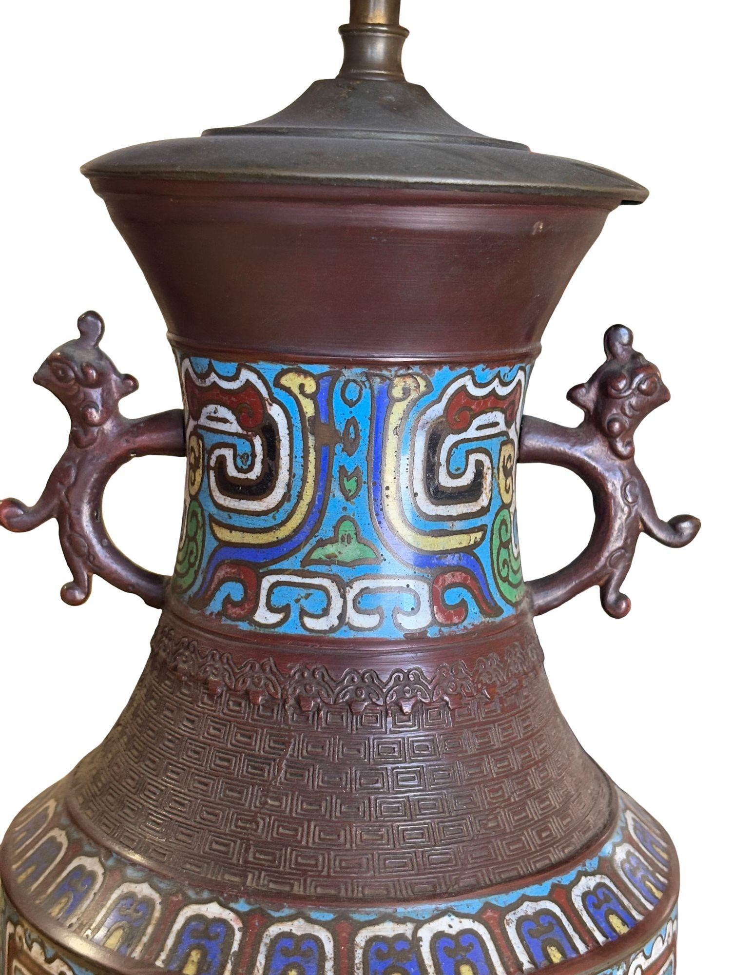 Cette lampe de table de la période Meiji des années 1910 présente une base de vase en émail cloisonné japonais avec de vifs motifs traditionnels et des poignées en forme de dragon. Surmonté d'un abat-jour en forme de dôme orné de volutes en fer