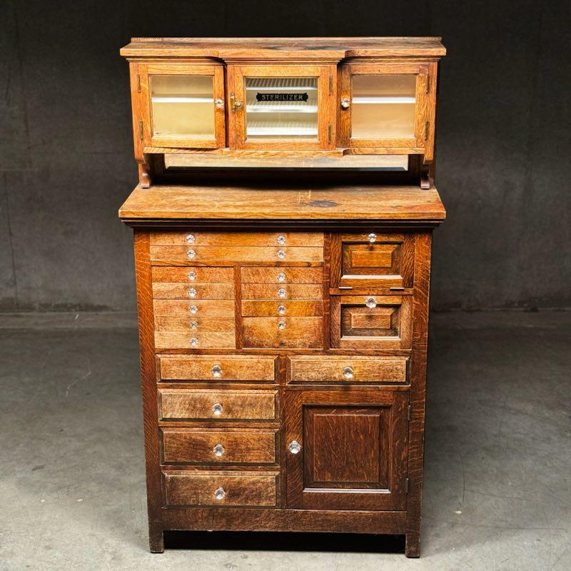 A totally original solid tiger oak dental cabinet in old worn finish as found stored for 50years. All hardware is original, fully locking trick drawer with original glass , bevelled mirror  and sterilized window.

Made by American oak cabinet Co. 

