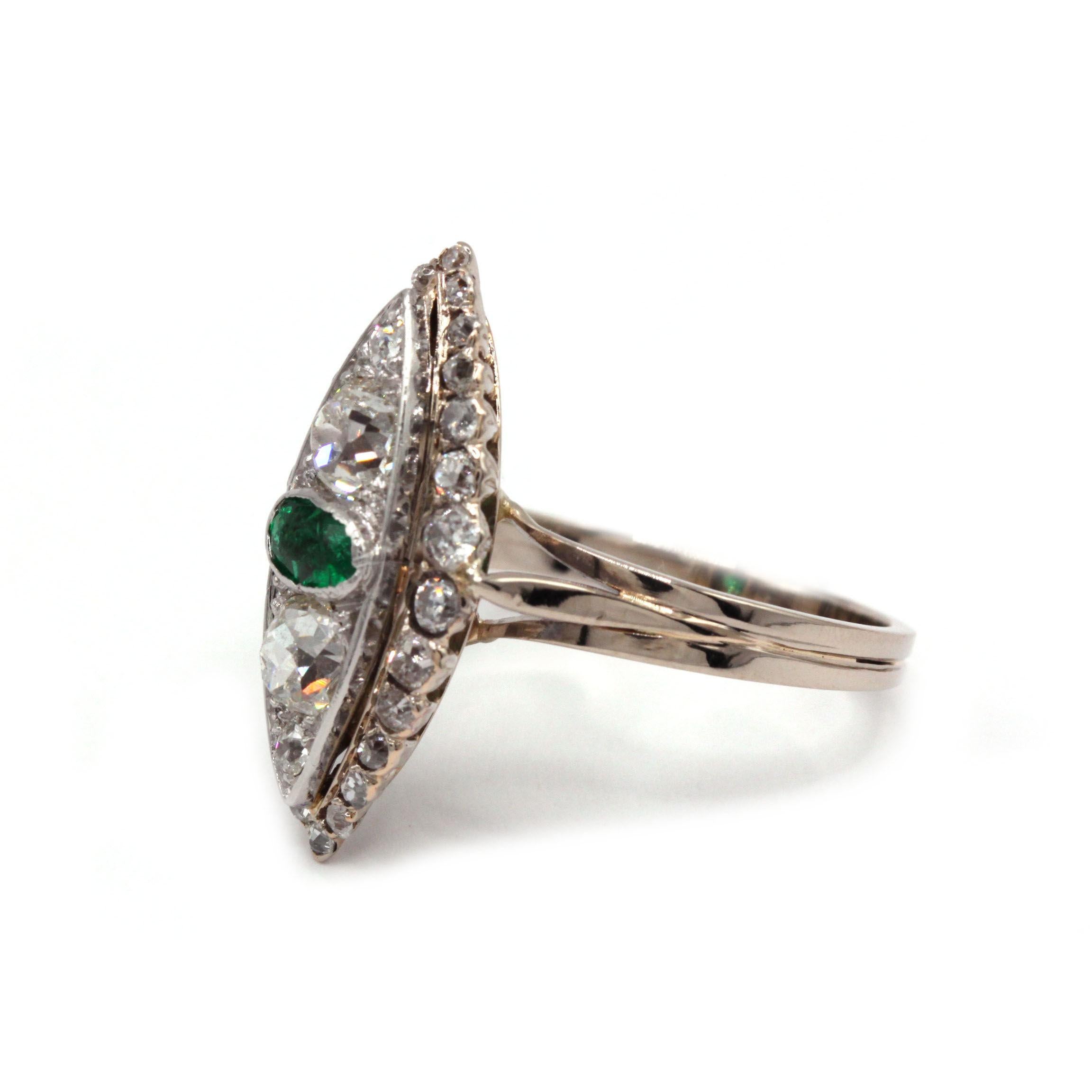 A striking example of early 20th-century French Art Deco jewelry, this marquise-shaped cocktail ring centers on an oval-cut emerald (~0.50 ct) flanked by two old European-cut diamonds (~0.60 ct each) and edged with a halo of 28 antique rose-cut