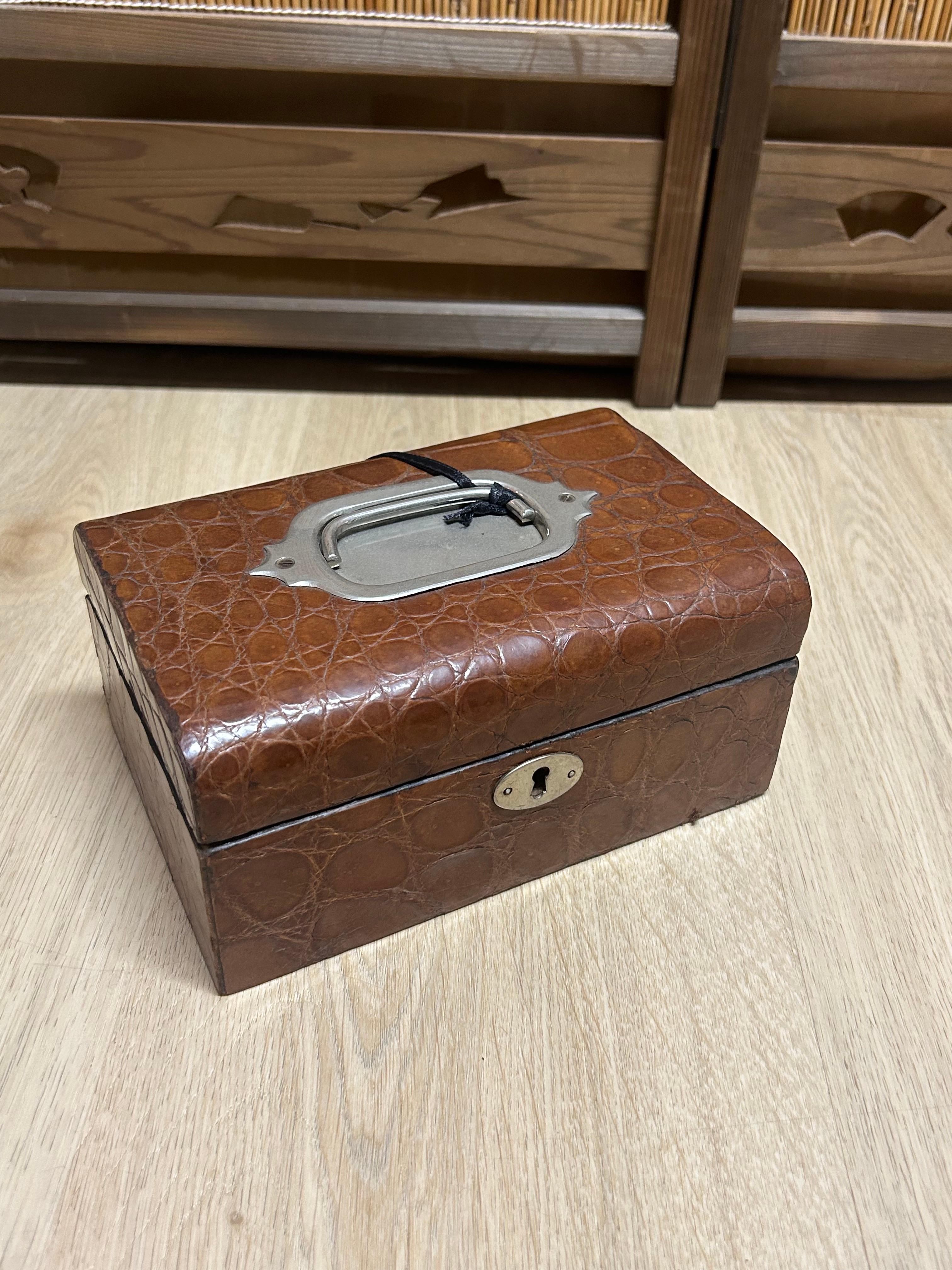 Small Alligator Jewellery box, containing a small removable tray for jewellery. On the centre of the lid a metal handle is attached, This box should have been a a travelling jewellery box, unfortunately the key is long gone.

The pictures are part