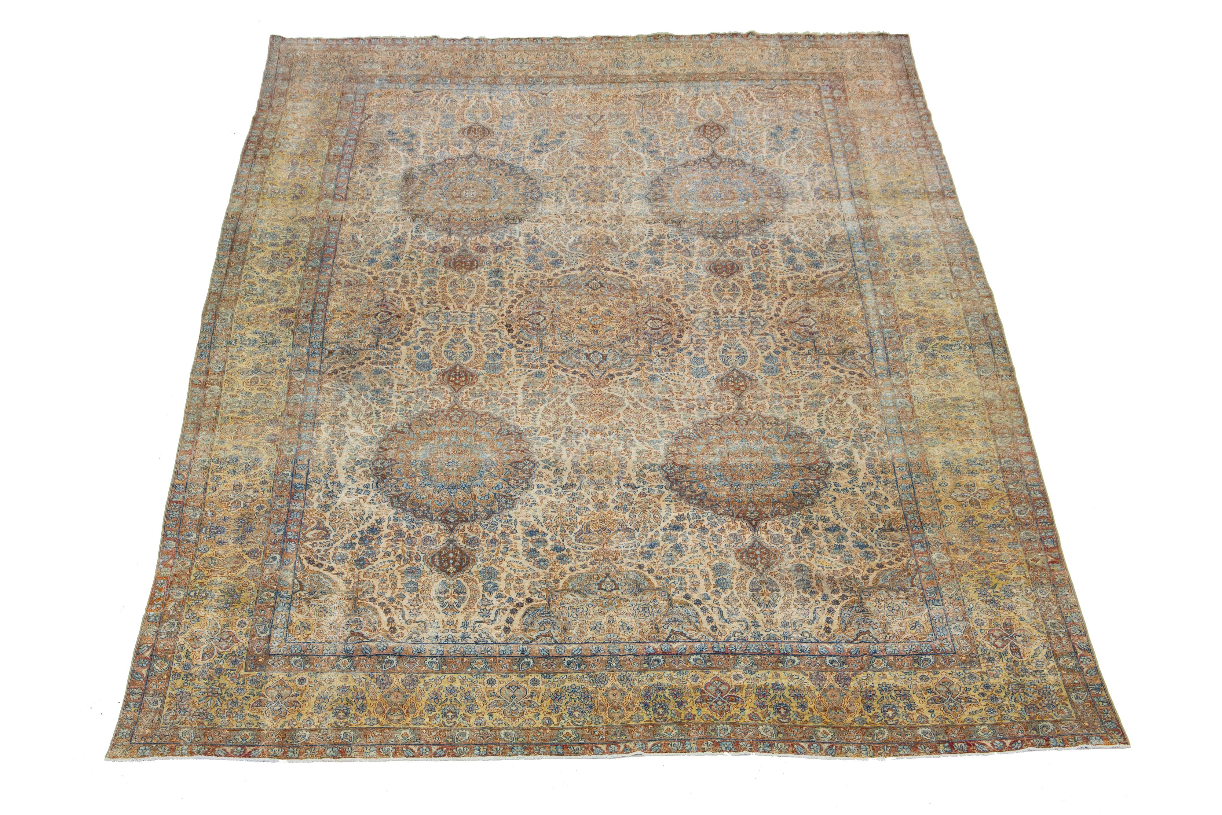 This exquisite, hand-knotted wool rug from Kerman boasts a charming antique finish. The rug's warm beige-tan color field is adorned with a stunning, all-over rosette pattern, highlighted by hints of rich blue and rust—a remarkable piece of Persian
