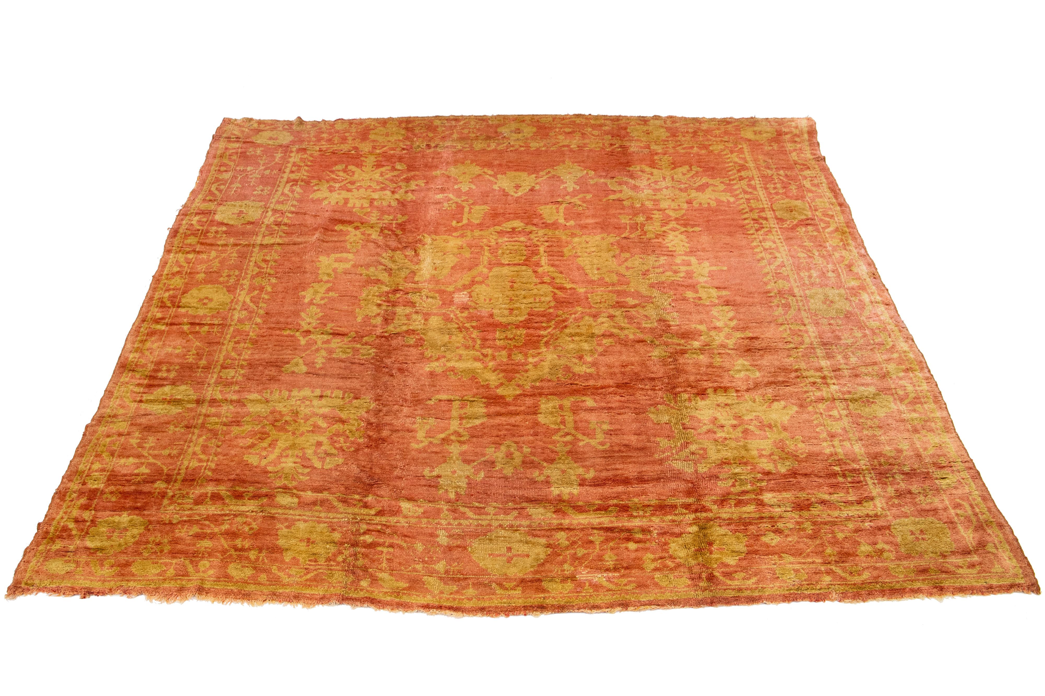 This antique Turkish wool rug from the 20th century features a charming terracotta-colored base and is meticulously hand-knotted with great attention to detail. It showcases stunning tan-golden accents that display a captivating floral