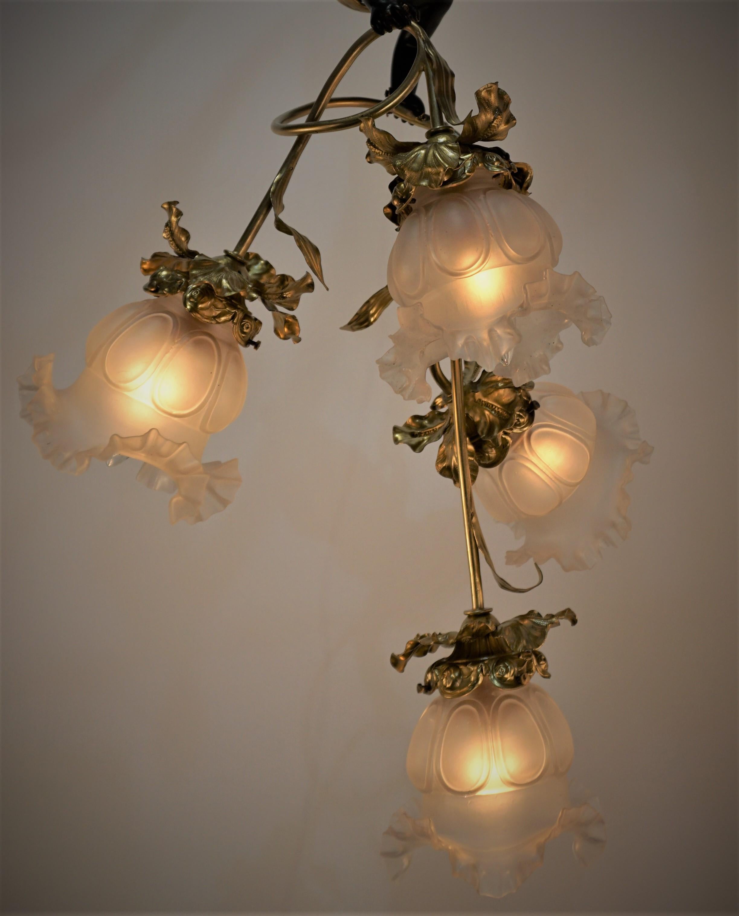 Handcrafted in France during the 1910's, this gorgeous chandelier features hand blown glass shades and oxidized cherub centerpiece. Beautiful organically inspired bronze detail work can be found throughout the chandelier, characteristic of classic