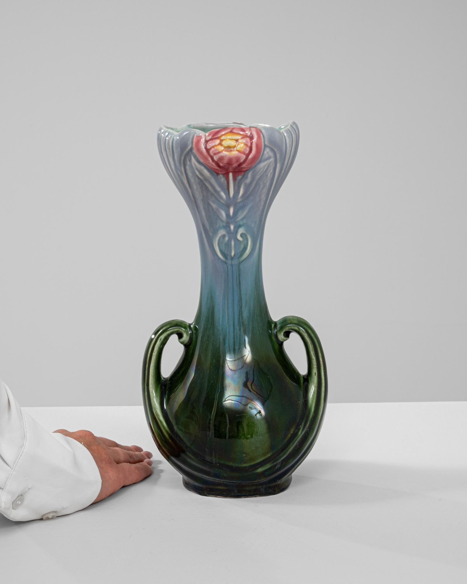 Questo squisito vaso in vetro belga del 1910 è uno splendido esempio di artigianato Art Nouveau, caratterizzato da un design fluido e organico ispirato alla natura. Le vibranti tonalità verdi e blu del vaso si alternano senza soluzione di