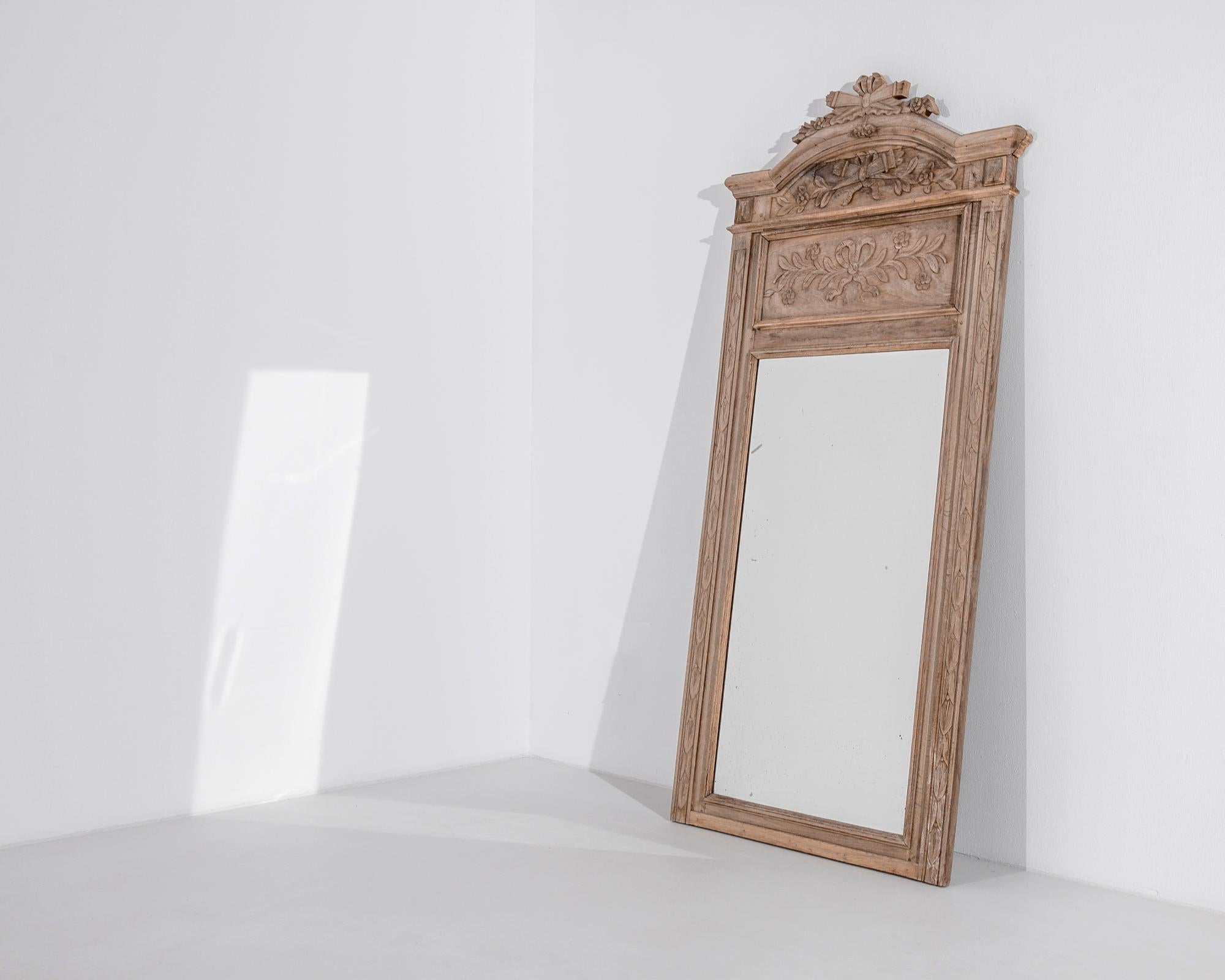 An oak floor mirror from Belgium, circa 1910, crowned by a majestic arch. Carved garlands of leaves and flowers tied with flowing ribbons give a verdant baroque touch. The rich russet tone of the oak, restored to a natural finish, gives a harmonious