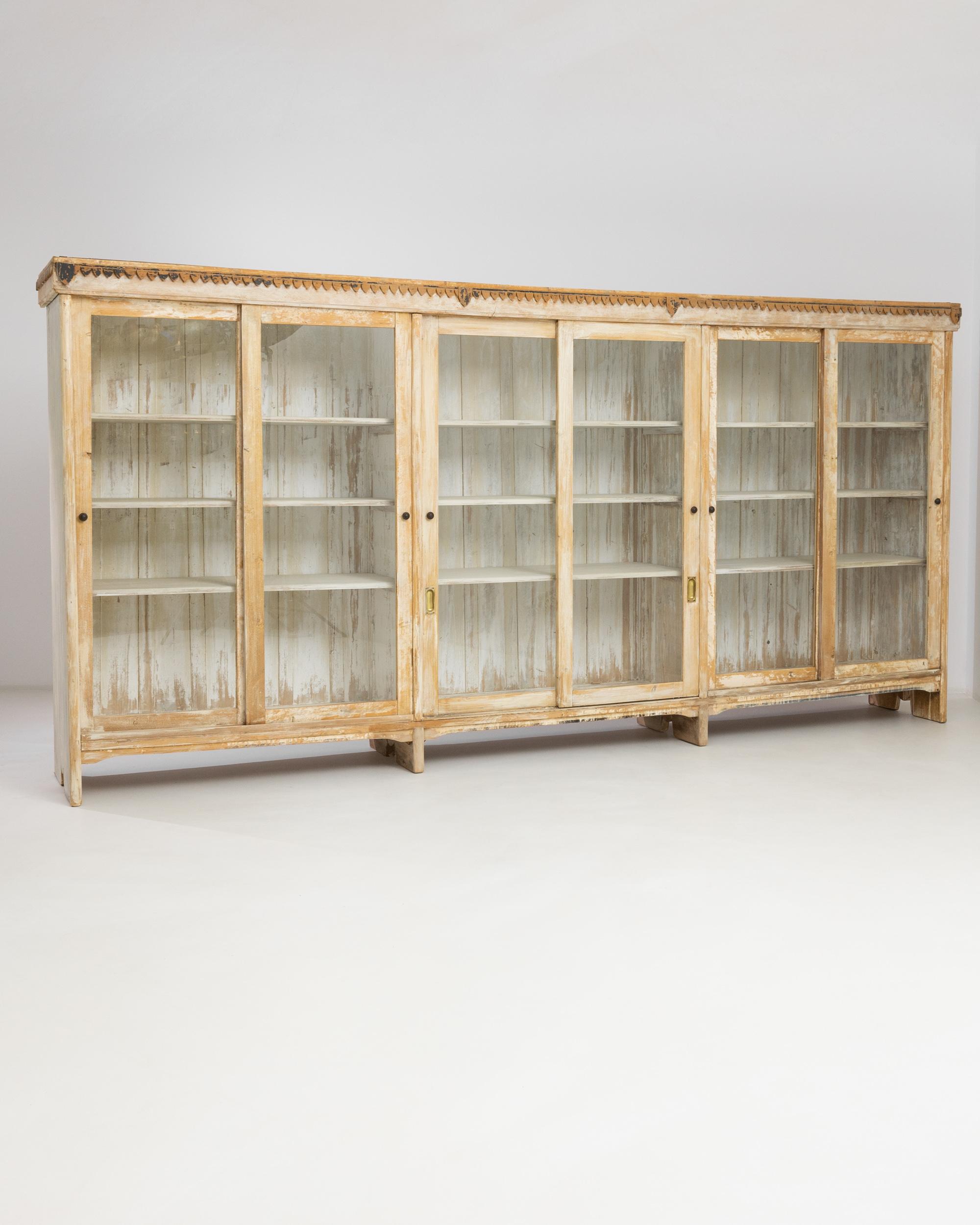 In a delightful nod to the past, this 1910s Central European White Patinated Wooden Vitrine unfolds its story across three distinct sections. Each of these segments reveals a pair of sliding glass doors, elegantly framing the treasures within. With