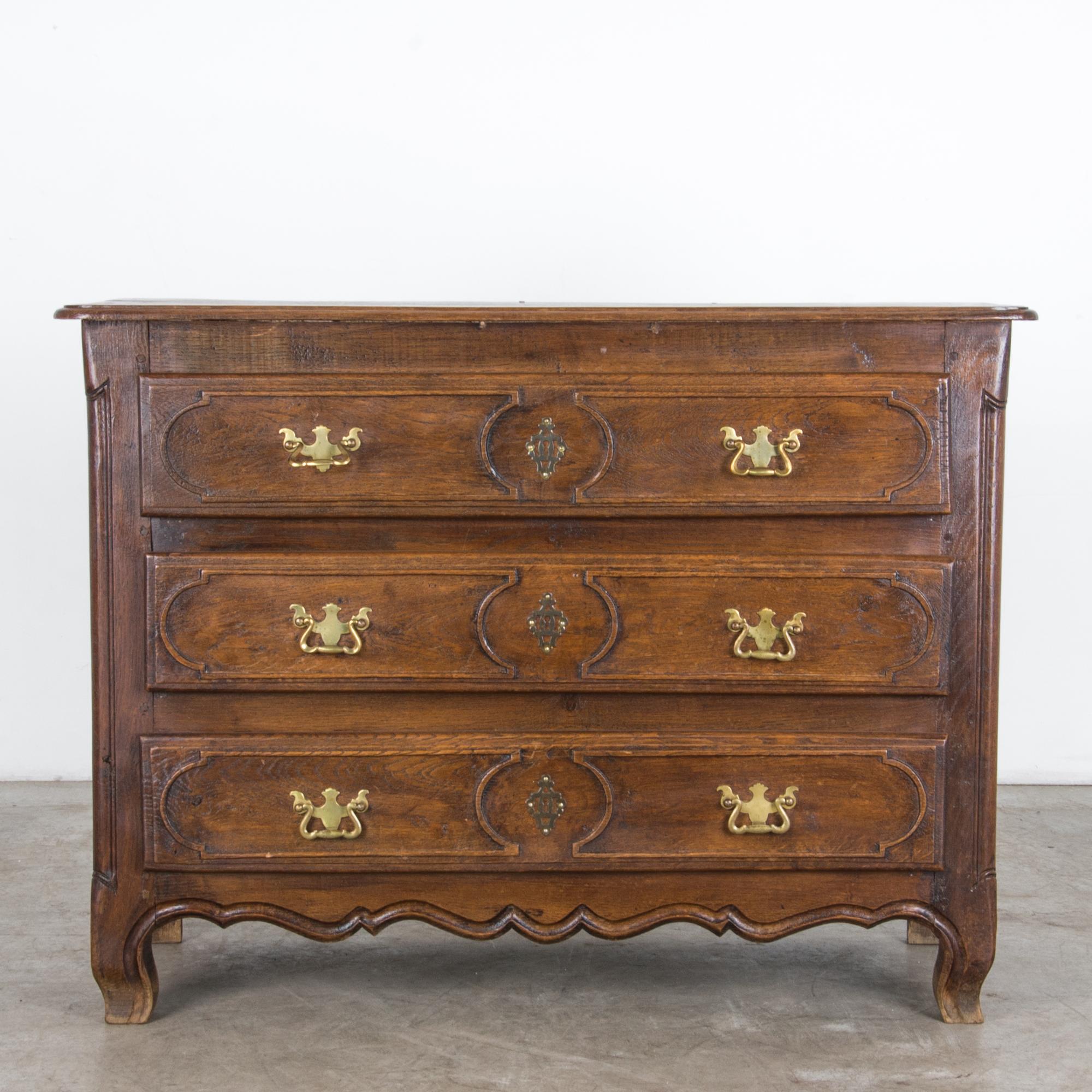 A chest of drawers from France, circa 1910. Brass fittings compliment a moody dark finish, with an inner warmth of textured oak. The elegant original finish suits the subtle carved detailing. A distinct approach typifies the casual yet refined