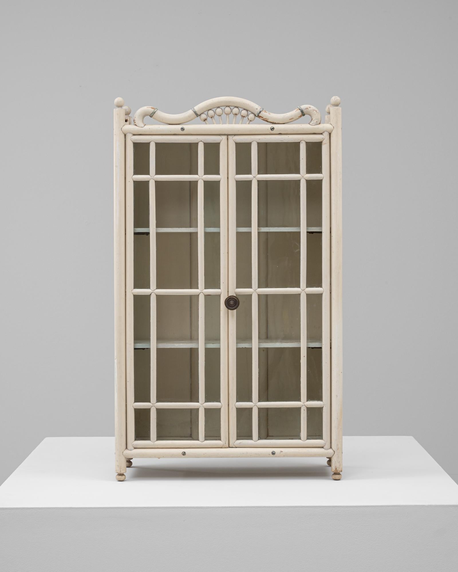 Questa affascinante mini vetrina francese in legno del 1910 cattura la delicata maestria del design dell'inizio del XX secolo. Dipinto in una morbida tonalità crema con una patina delicatamente invecchiata, presenta doppie porte con vetri