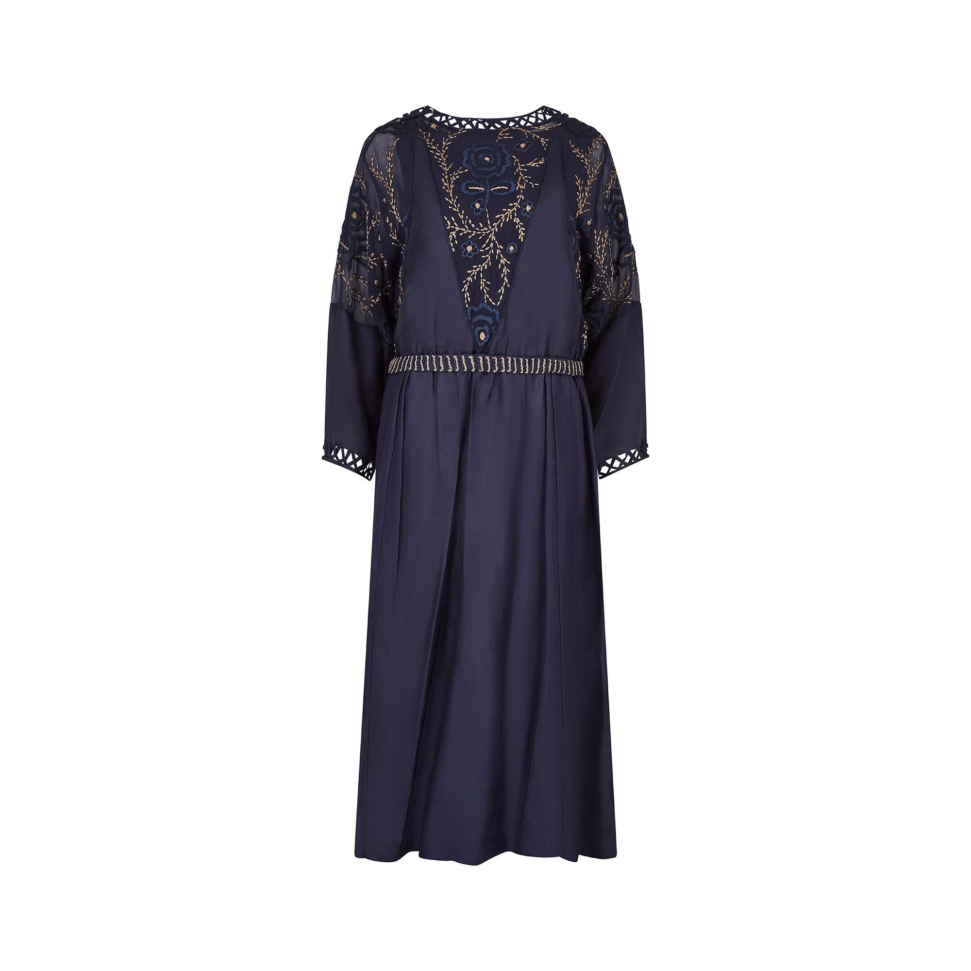 This is an incredibly well preserved midnight blue silk dress, dating from the late 1910s to the early 1920s. It features a softly rounded neckline, with a crisscross silk ribbon trim and six popper closure to the right hand neck seam. The front and