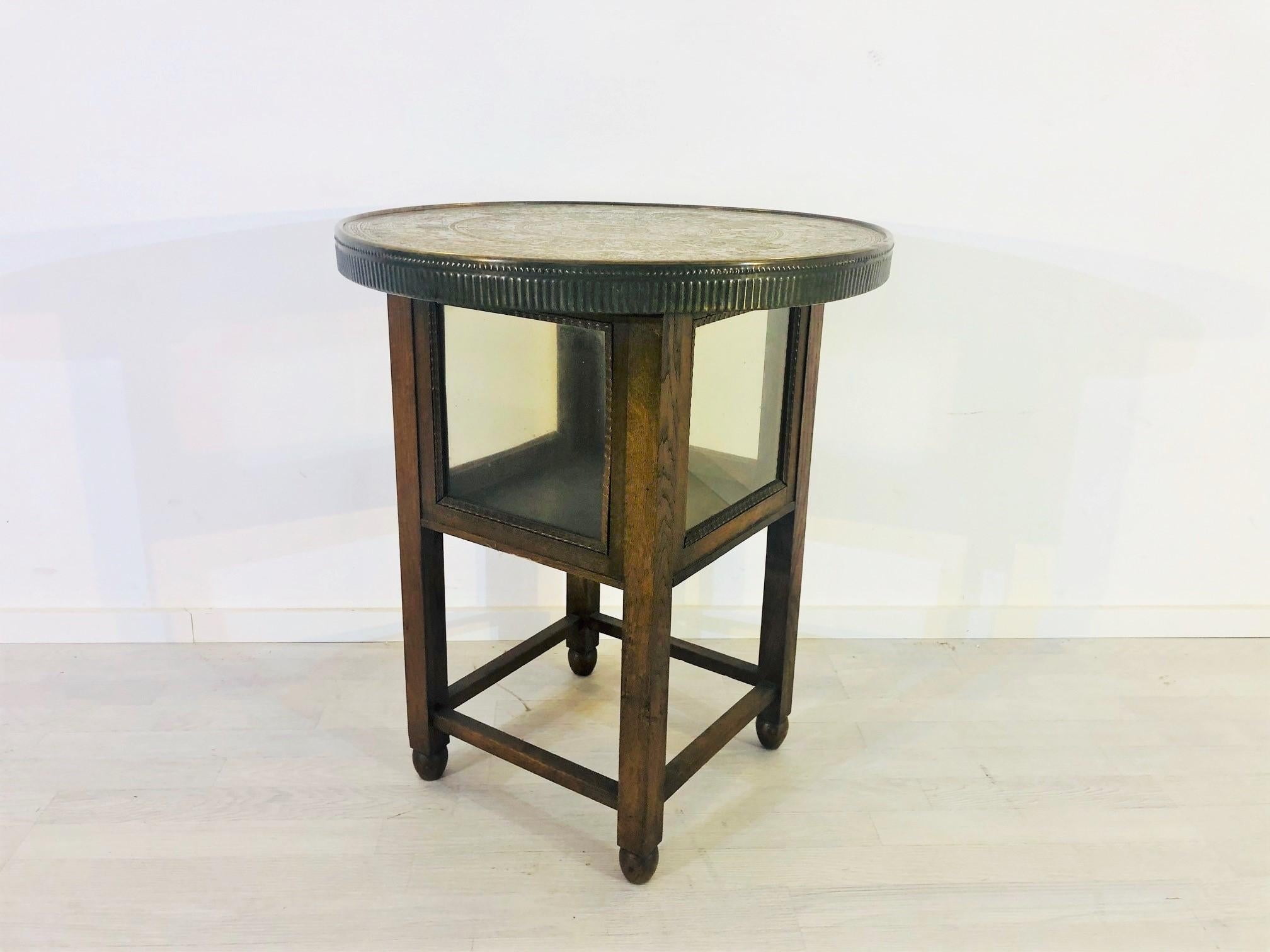 Original 1910s historicism side table with a brass tabletop and a small glass vitrine compartment below it. The beautiful tabletop is ornamented with stunning Egyptian hieroglyphics which is typical for the historicism era in the early 20th century.