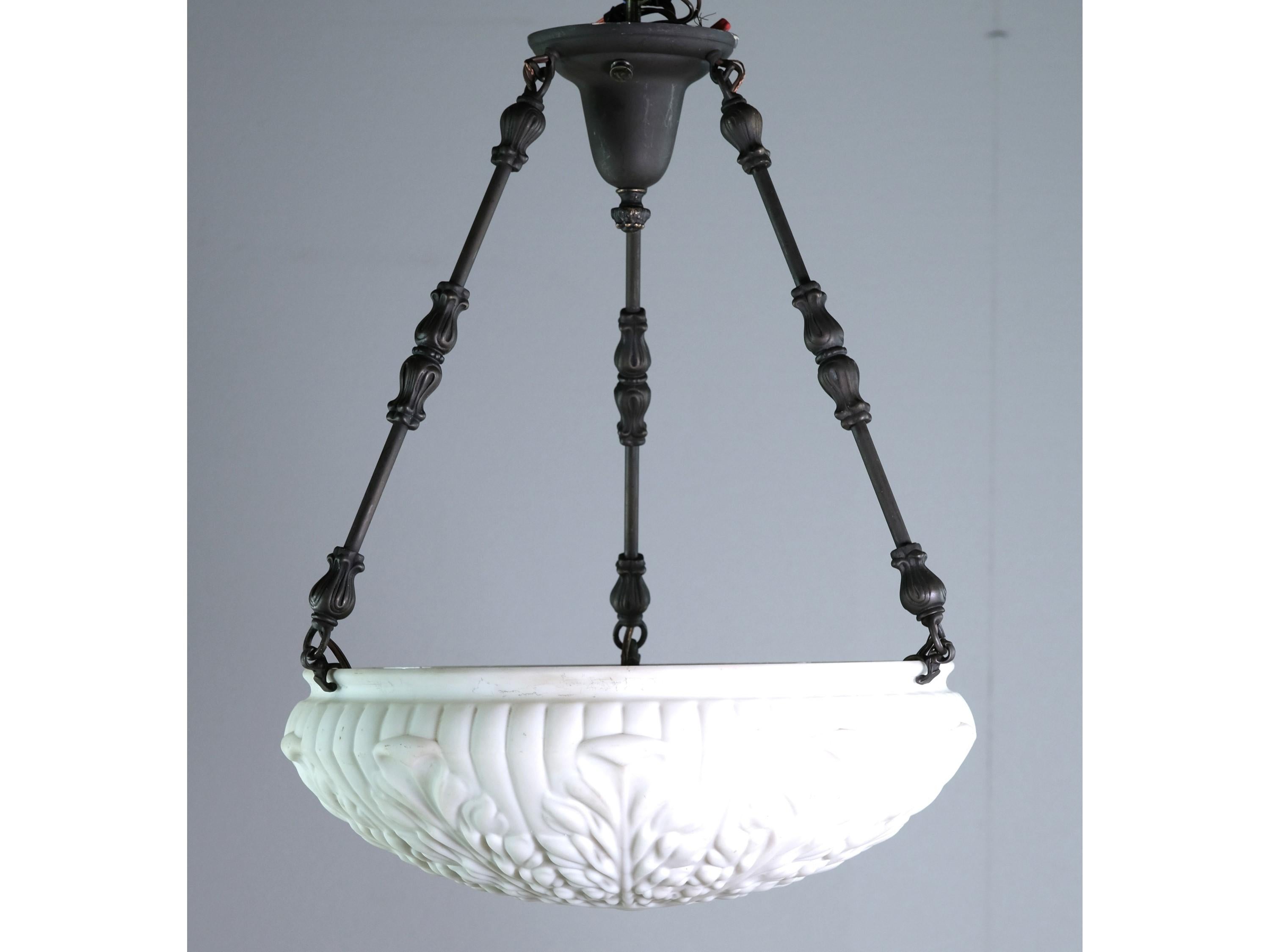 1910s Milk glass pendant dish light with a decorative three pole fixture. The dish is heavily embossed with foliage details and has a bisque color. The three pole fixture is in a charcoal finish. The price includes restoration. This can be seen at