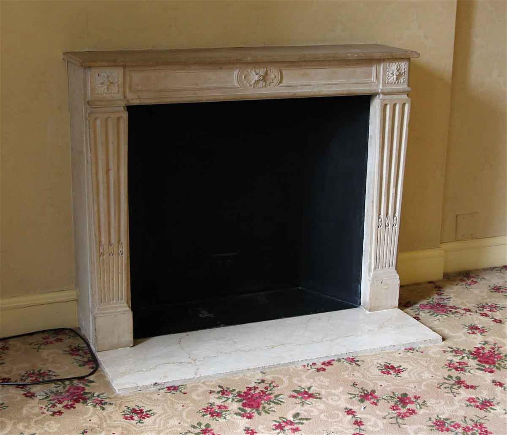 1910s Louis XVI French Regency style tan limestone mantel. Carved legs and floral motifs on the top plinths and the middle of the header. This mantel was one of a group of antique mantels imported from Europe and installed in the NYC Waldorf Astoria