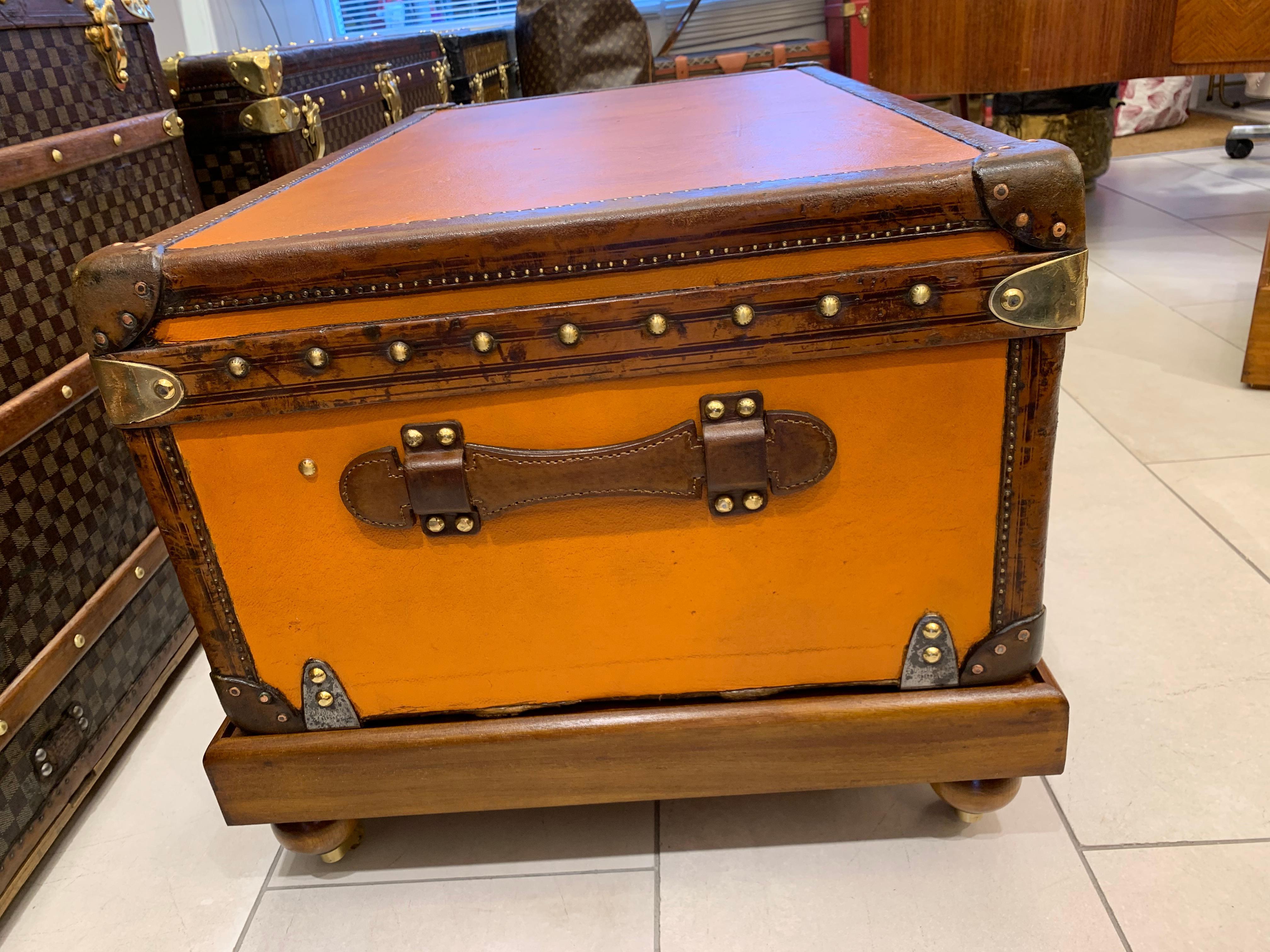 Cette malle Louis Vuitton peu commune présente une belle toile orange, des garnitures en cuir de couleur chocolat, de grandes poignées latérales en cuir, ainsi qu'une serrure, des fermoirs et des clous en laiton estampillés Louis Vuitton. Il a une