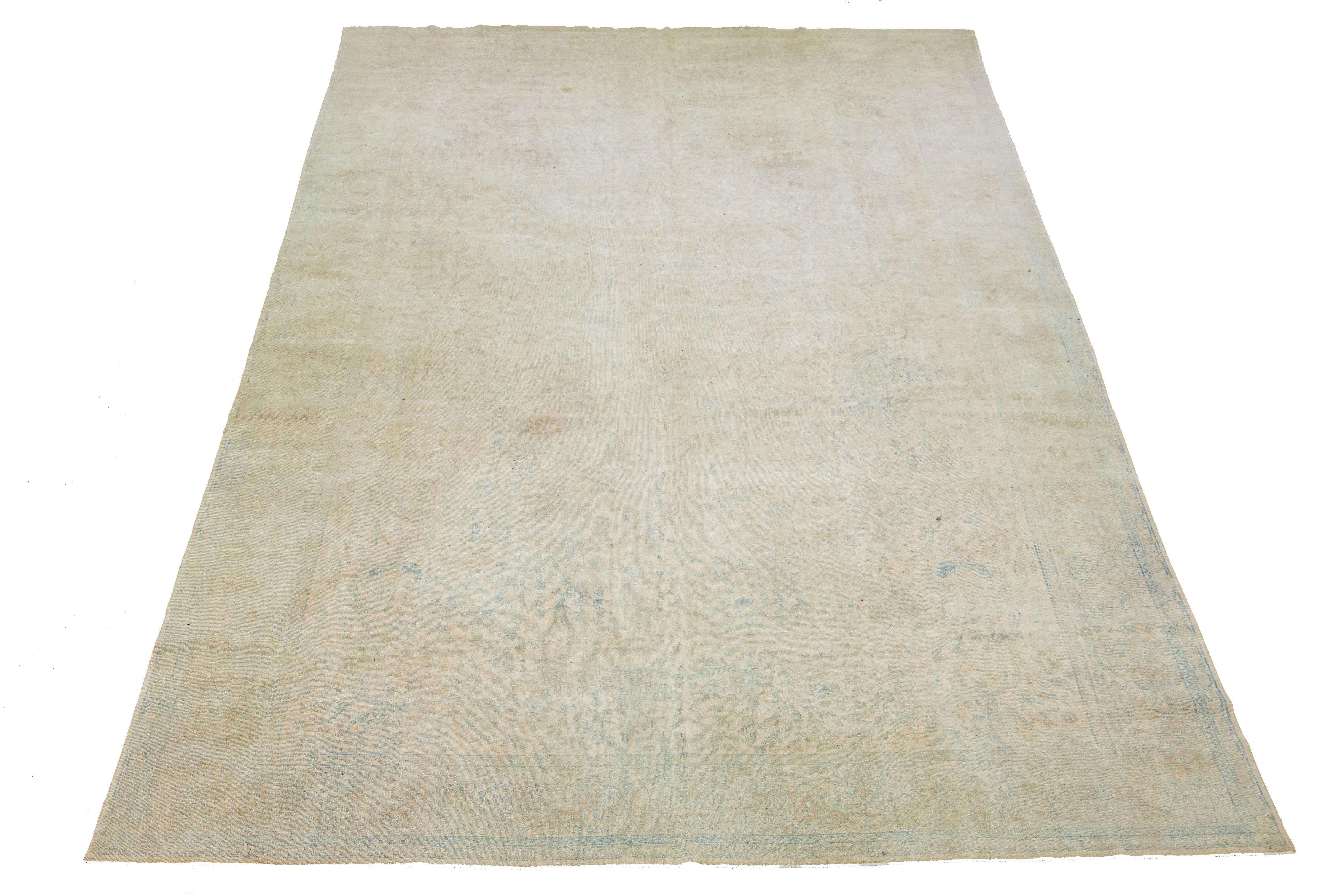 This beautiful hand-knotted, antique Agra wool rug has a tan-beige color field. The rug hails from India and features blue and brown accent colors in an all-over floral design.

This rug measures 10'9