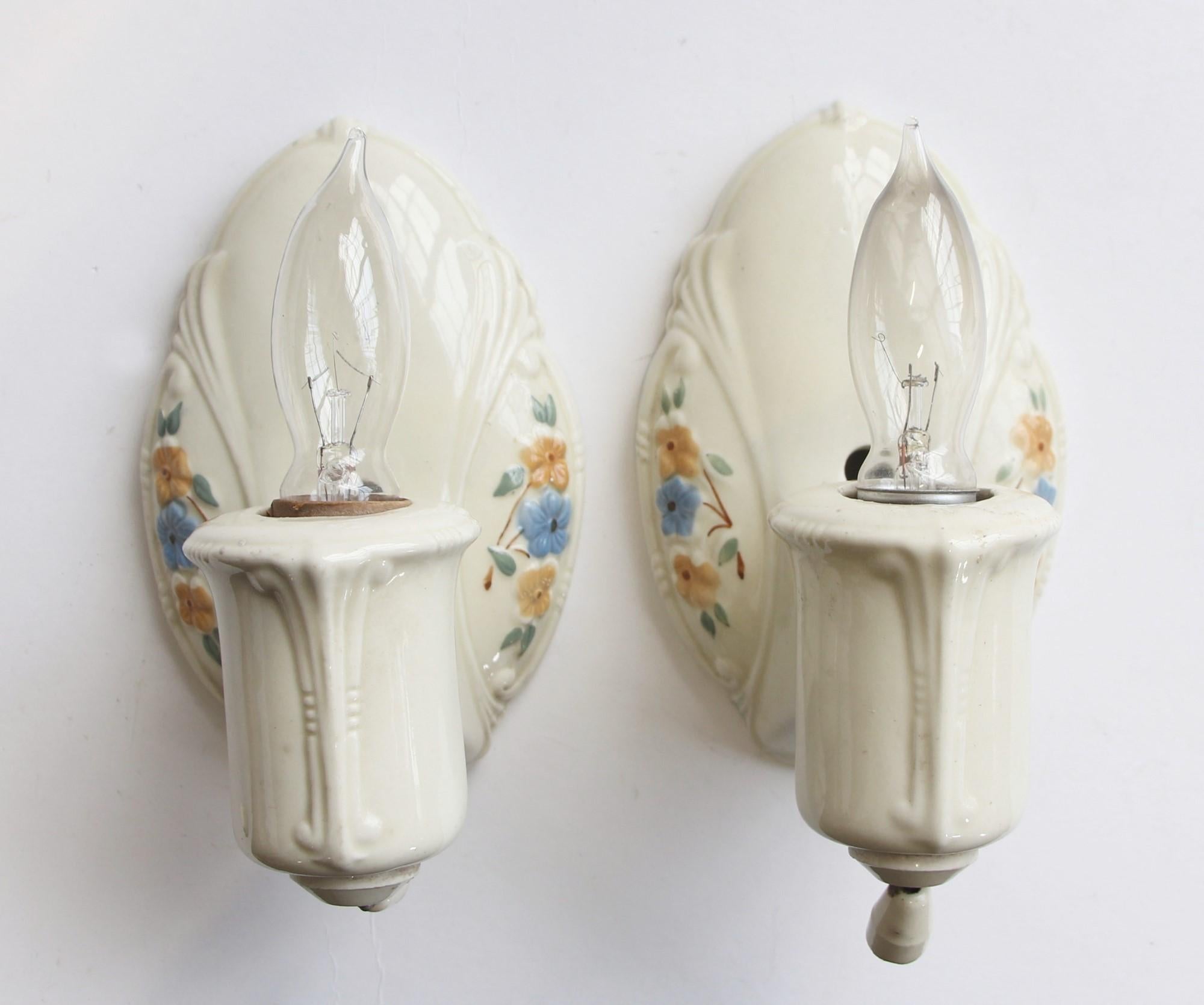 Antique 1910s pair of white ceramic porcelain sconces. Done in a floral pattern of orange and blue flowers with green leaves. Priced as a pair. These will be rewired before shipping. This can be seen at our 400 Gilligan St location in Scranton, PA.