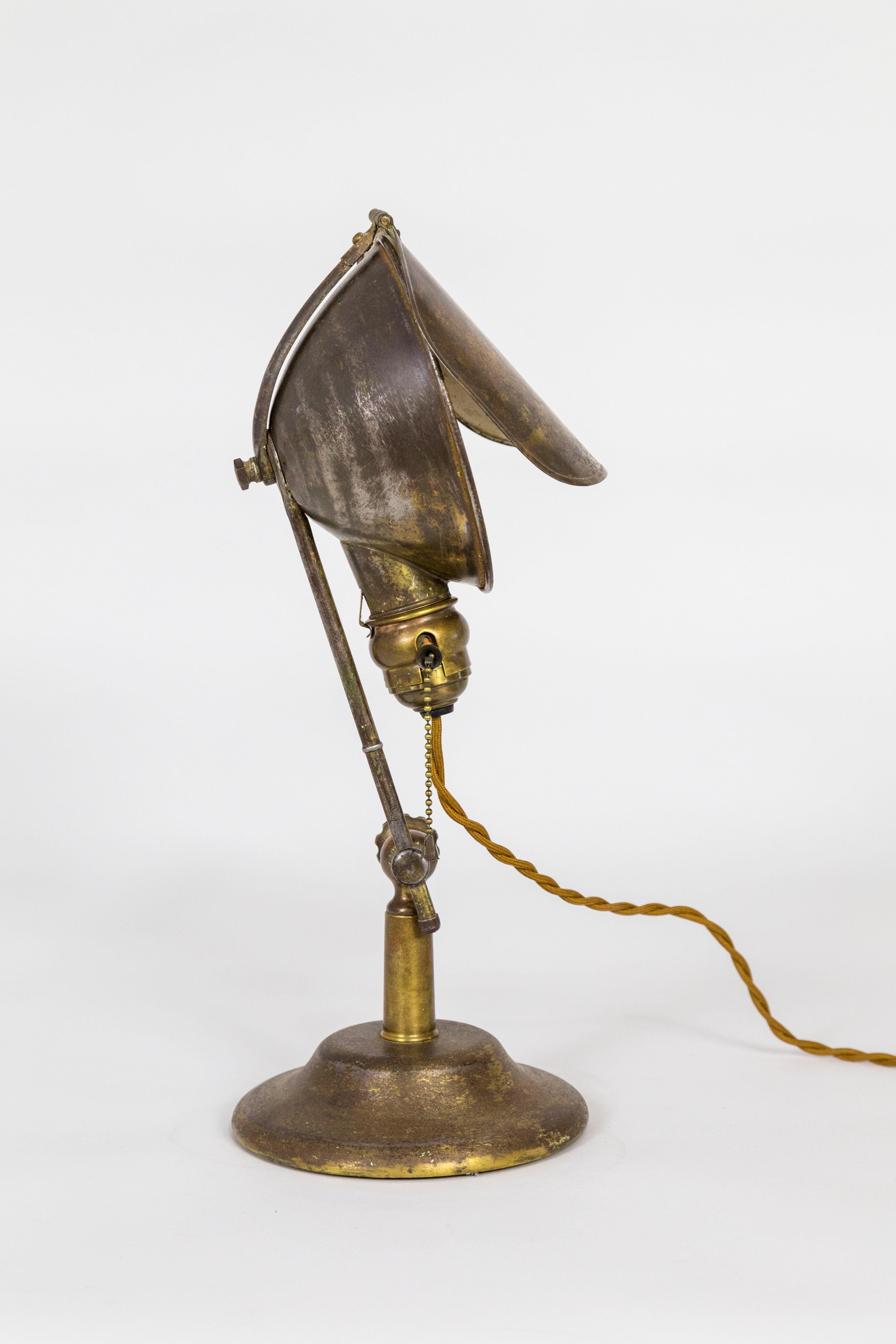 An early 20th century, Industrial task lamp with clamshell shade and distinctive, rotating glare guard. Made by Anker Storm Lyhne and Beers Sales Co. of Bridgeport, Connecticut in the 1910s, this patinated brass lamp is highly adjustable with a