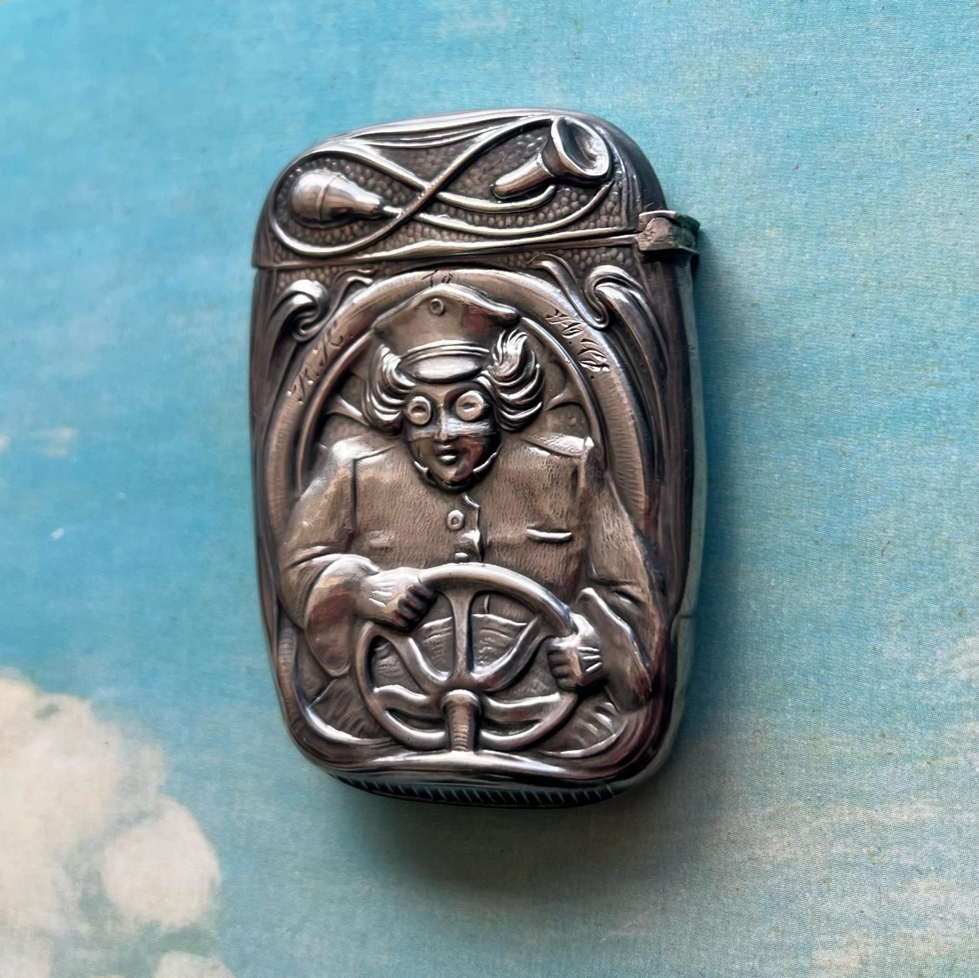 A striking and highly detailed sterling silver match safe, this c. 1910s example attributed to Blackinton features a bold raised depiction of a whimsical chauffeur gripping a steering wheel, complete with flying hair, goggles, and uniform. The lid