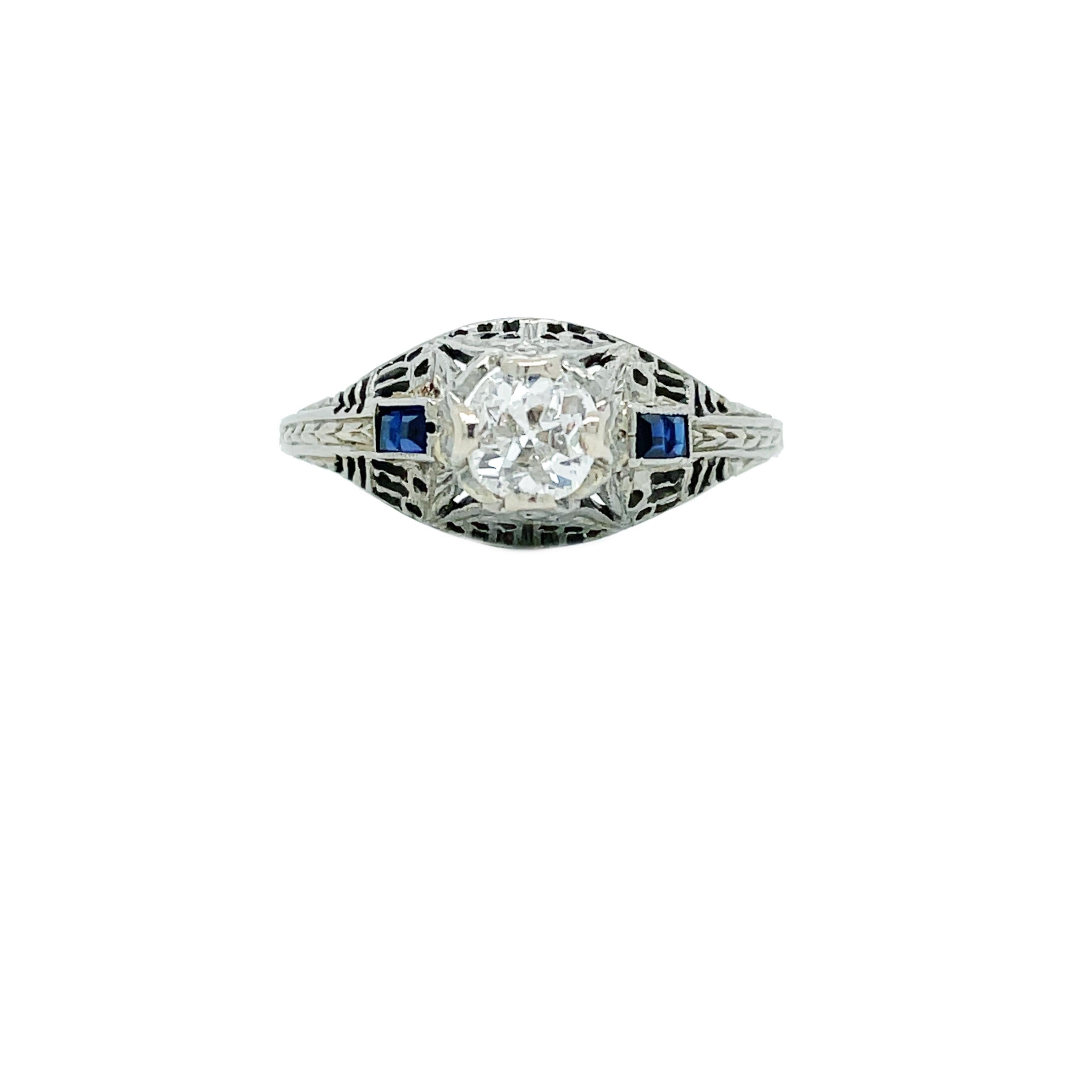 This is a lovely Art Deco 18K white gold ring showcasing a gorgeous icy white old mine cut diamond with vivid blue square synthetic sapphires on the shoulders. This is a stunning example of classic Art Deco jewelry! Set by 4 18K white gold prongs at