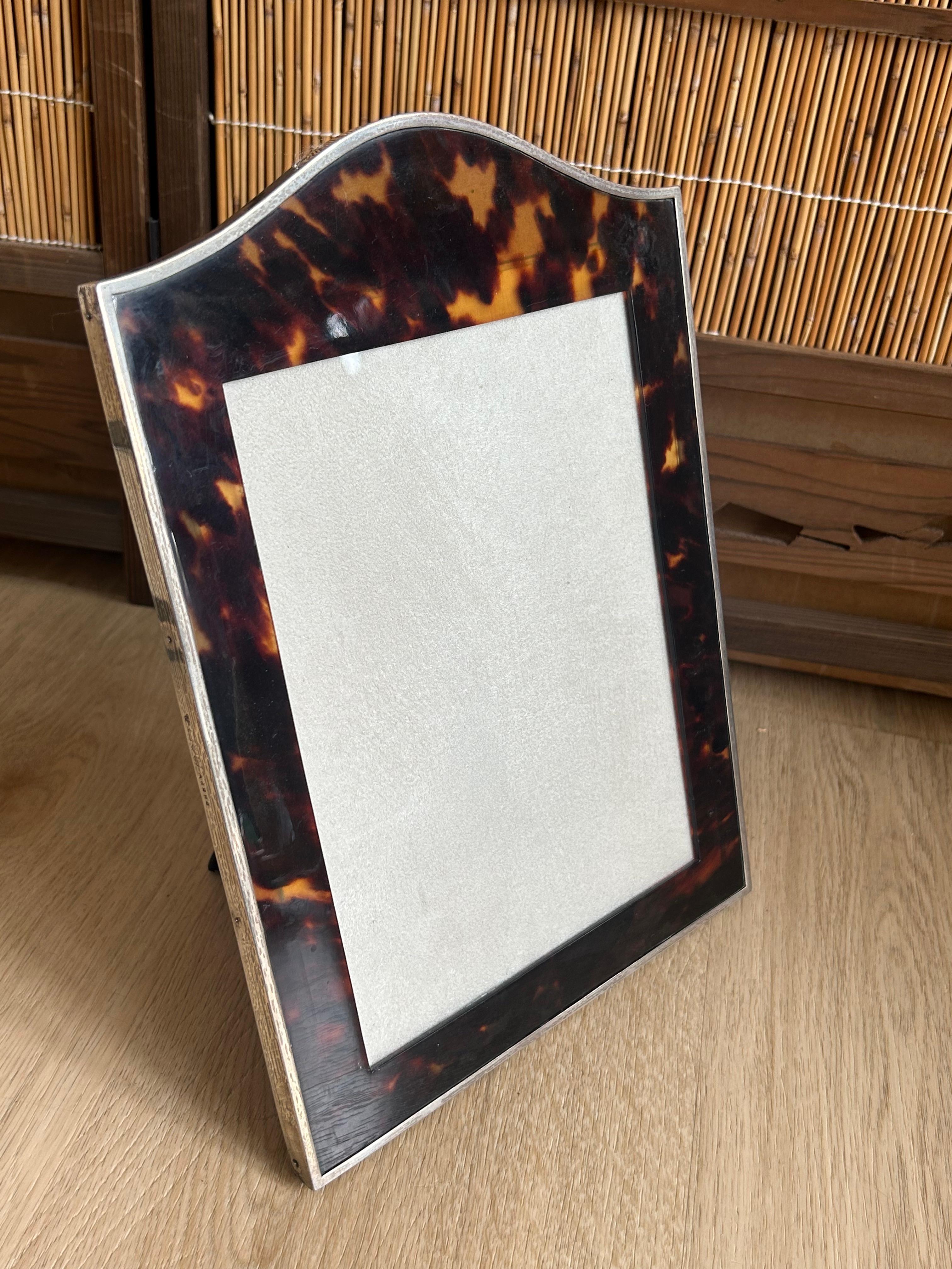 One tortoiseshell Photograph Frames with silver rims and suede backings.
 A Photograph Frame with arched top and silver rim,  black material backs, London 1915, numbered A6292, mark of C&RC for Charles Reynolds & Co,

The pictures are part of the