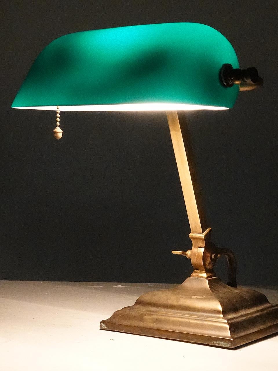 The lamp is unsigned but the glass tells me it must be a Verdelite. these lamps mostly date to the very early 20th century. This banker's desk lamp or piano lamp has an original emerald green blown glass shade.