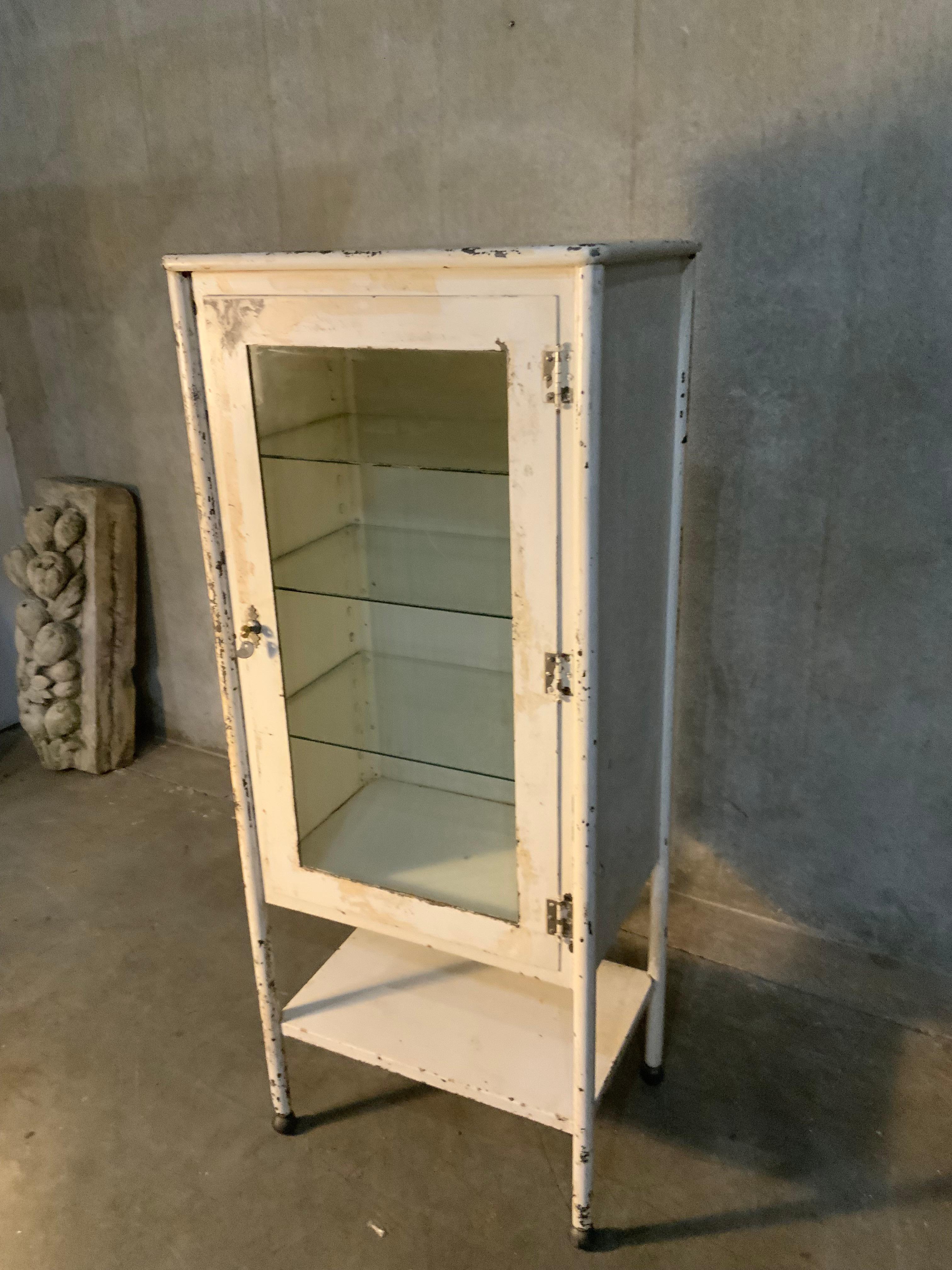 This medicine cabinet was produced in the 1920 in the USA by Reid Bros. , based in Santa Francisco/ Seattle. It is made from thick iron and antique glass. With a very nice original lock and handle on the top door. 
It features four adjjstable glass
