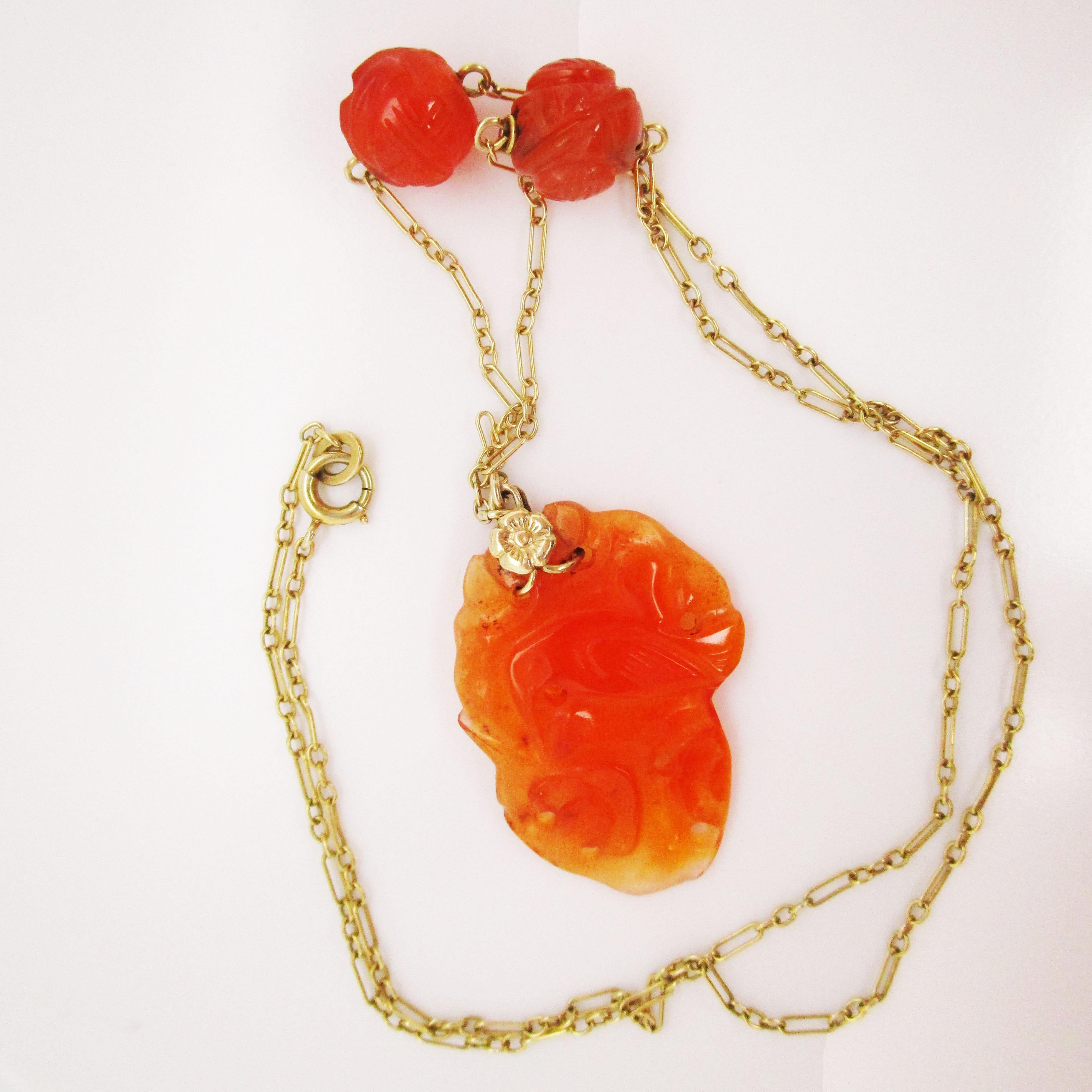 This stunning necklace is a fantastic example of Art Deco from 1920 and features a lovely combination of 14k green gold and rich orange carved carnelian. The center of the necklace is a carved carnelian with a fascinating asymmetrical shape with an