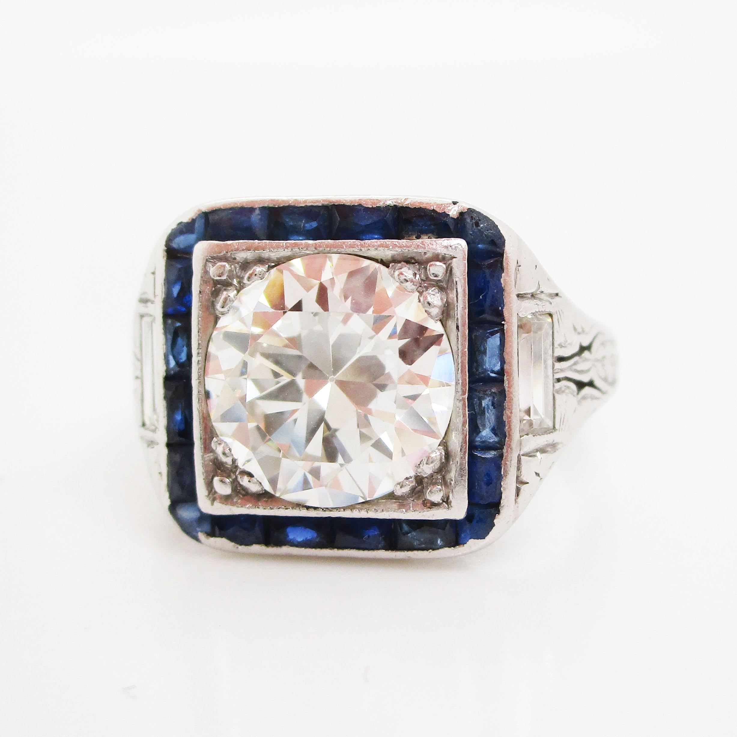 This is a stunning original Art Deco ring in platinum with a beautiful white diamond center stone framed by French cut blue sapphires. The geometric layout and the contrast of white and blue creates a bold, elegant look that is distinctly Art Deco.