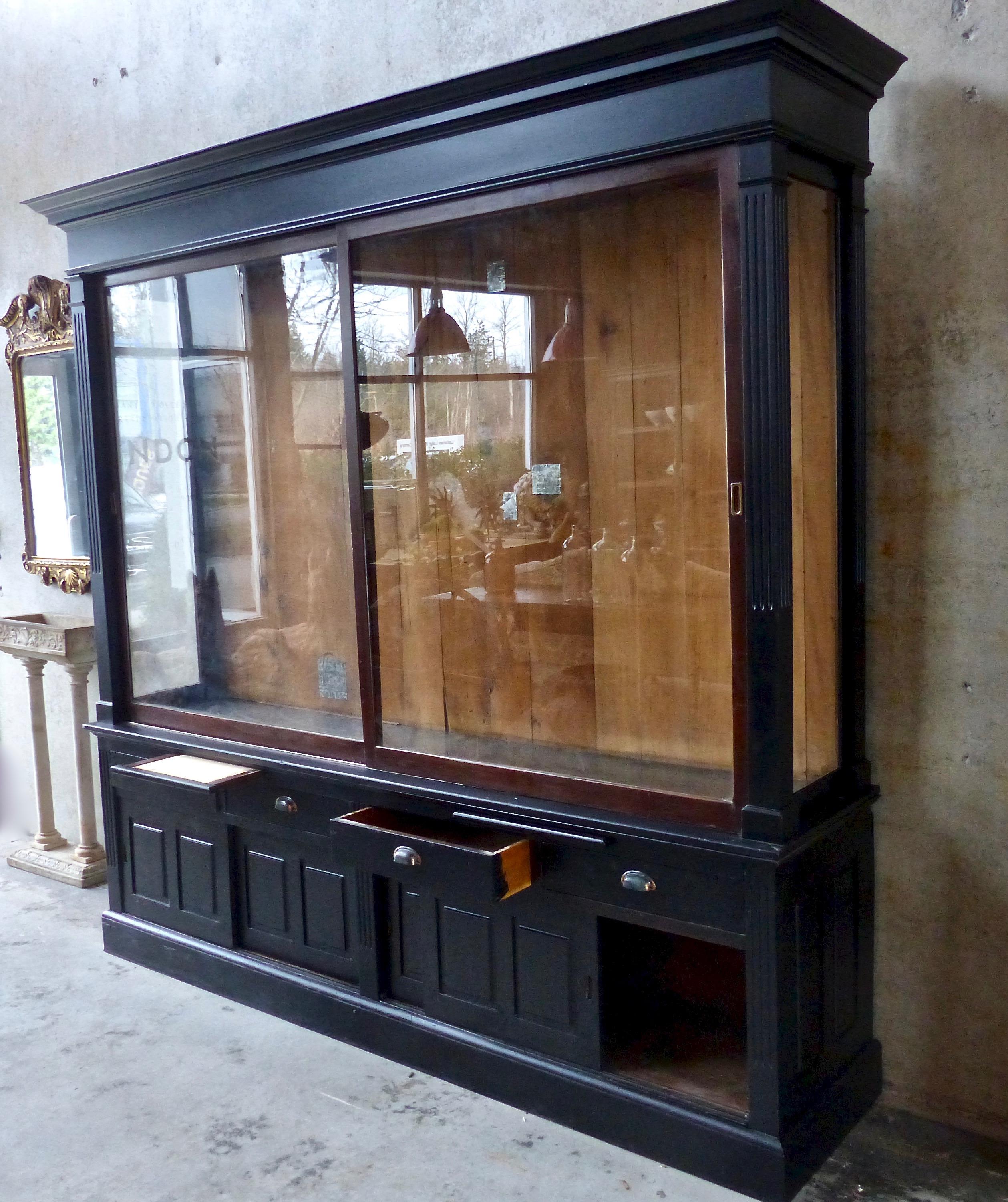 A stately Art Deco era mercantile display cabinet with upper sliding glass doors (approx. 7 H” x 4 W’) plus a lower enclosed section that features shelves, four drawers, and two pull-out ‘desktops’. Brass hardware and an elegant black finish. First