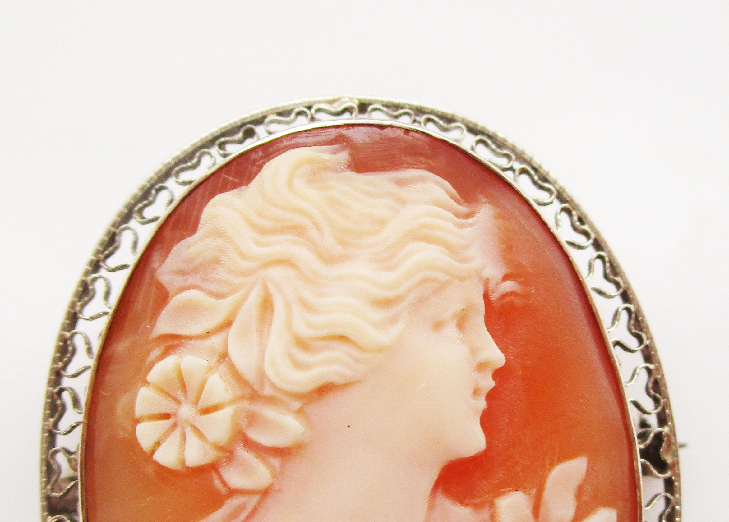 This is a gorgeous Edwardian three-color shell cameo set into a stunning 10k white gold frame with a lace-like detailing. The carving is absolutely beautiful, featuring the right facing portrait of an elegant Edwardian woman adorned with flowers.