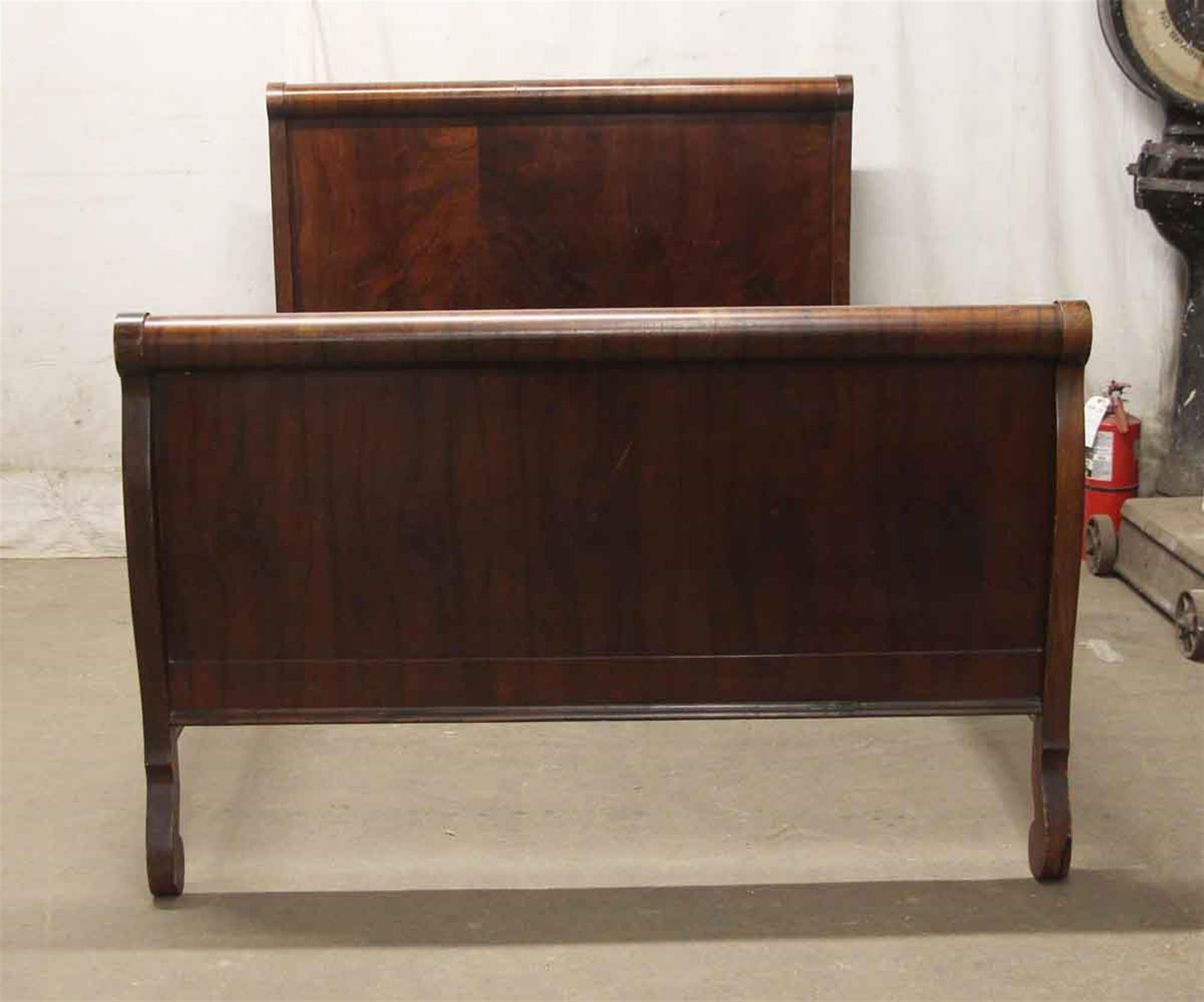 This bed frame is in the Craftsmen style and has a dark wooden tone. It is a full bed made of solid wood with a figured walnut veneer, circa 1920. This can be seen at our 400 Gilligan St location in Scranton, PA.
