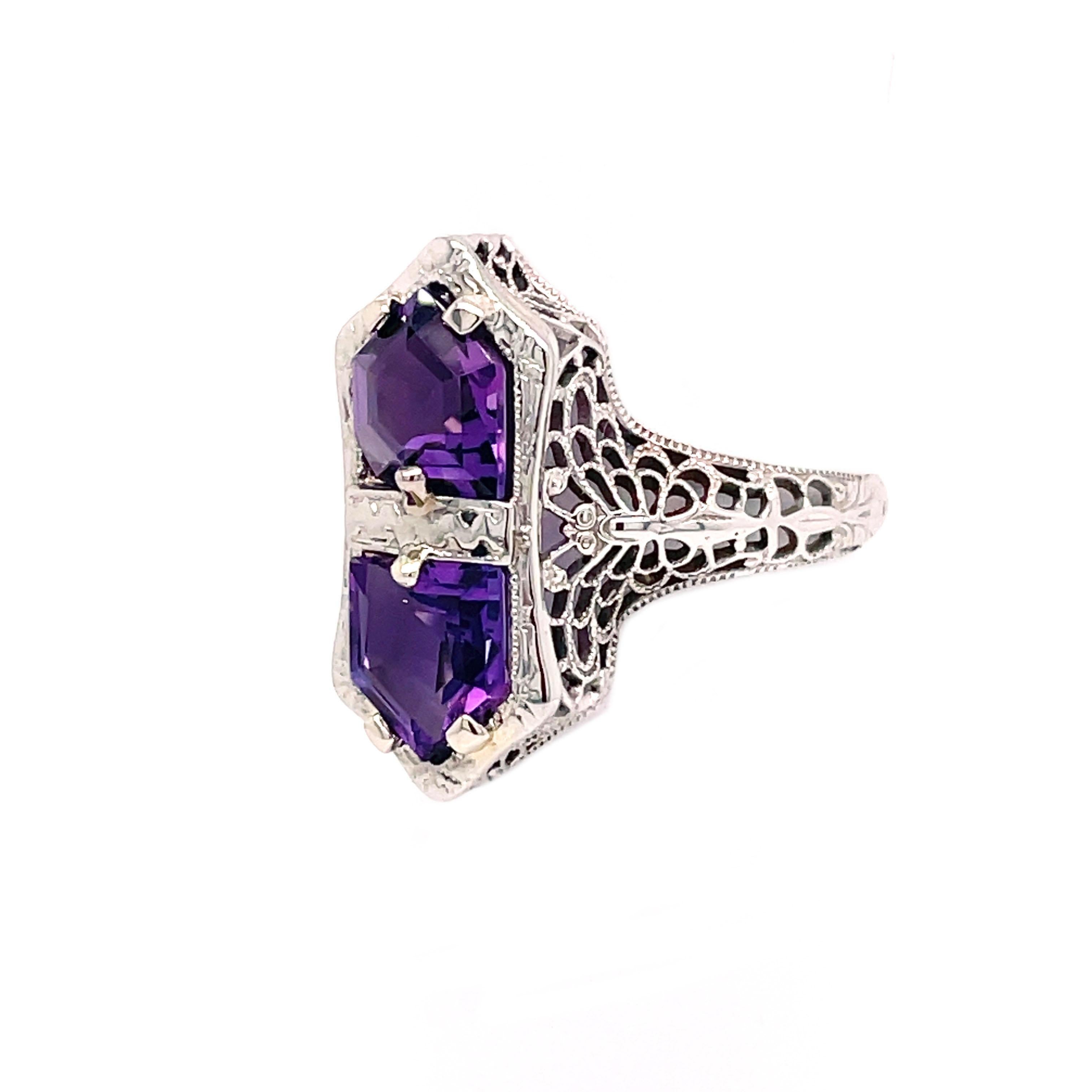 This charming 1920s filigree ring is set in 14K white gold with two beautiful rich purple amethyst! This whimsical ring is in pristine condition and features a lovely butterfly motif along the shoulders of the ring. The design of this ring is