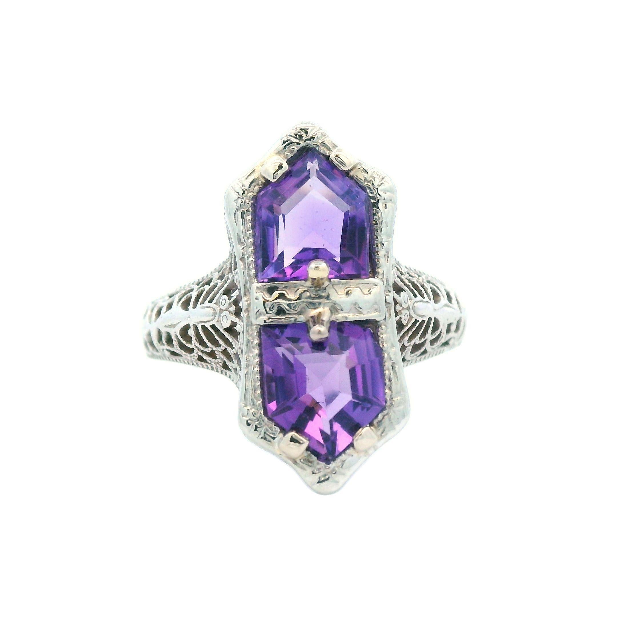 This delightful filigree ring from the 1920s is crafted in 14K white gold and showcases two stunning rich purple amethyst gemstones. The ring exudes charm and is in excellent condition, adorned with a whimsical butterfly motif along its shoulders.