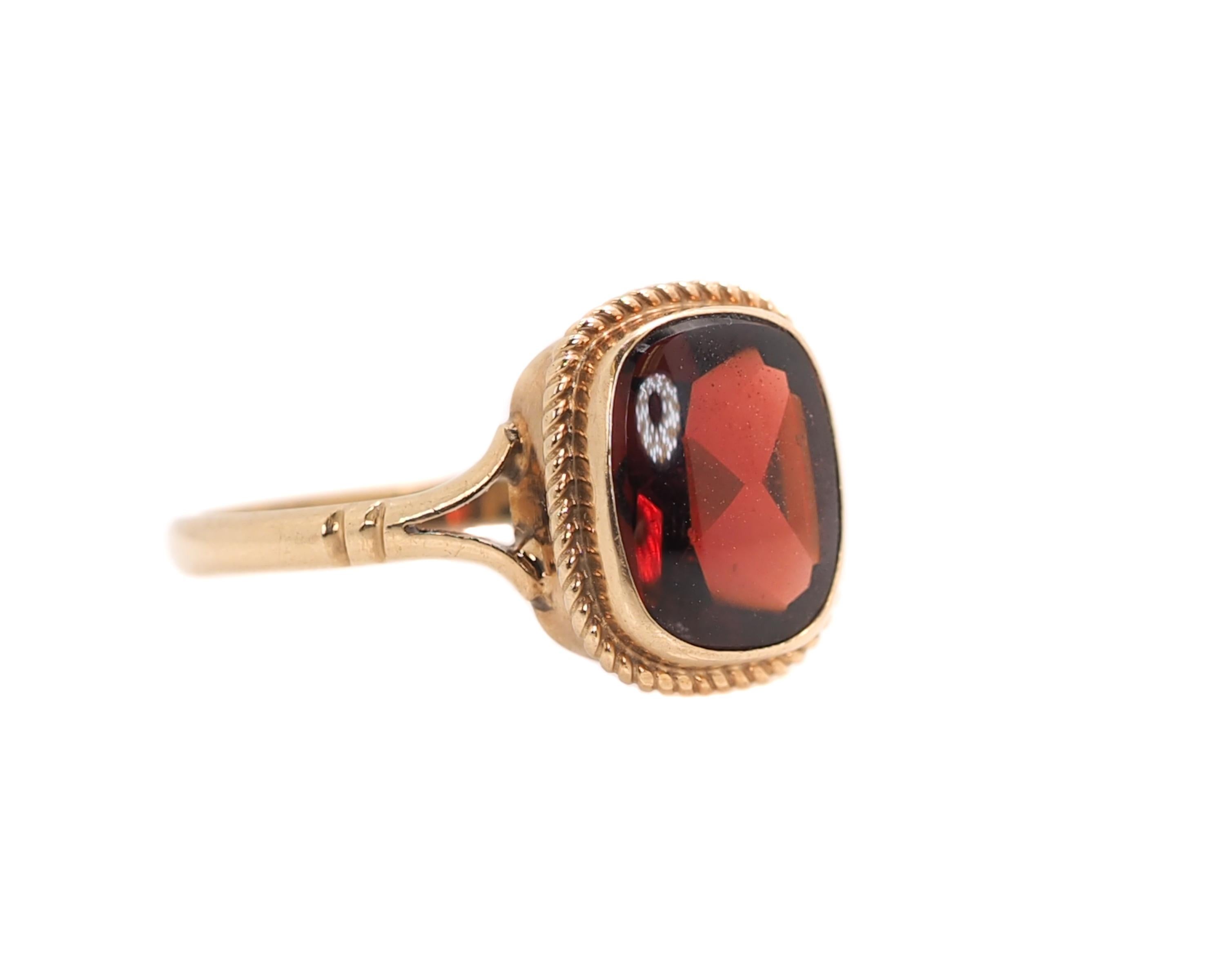 1920s Art Deco Red Cabochon Stone and 9 Karat Yellow Gold Ring

Features a Russian-Red, Cushion cut center stone bezel set in rich 9 karat Yellow Gold. 
A fine braided wire halo frames the bezel setting. The split shank shoulders lead to a smooth