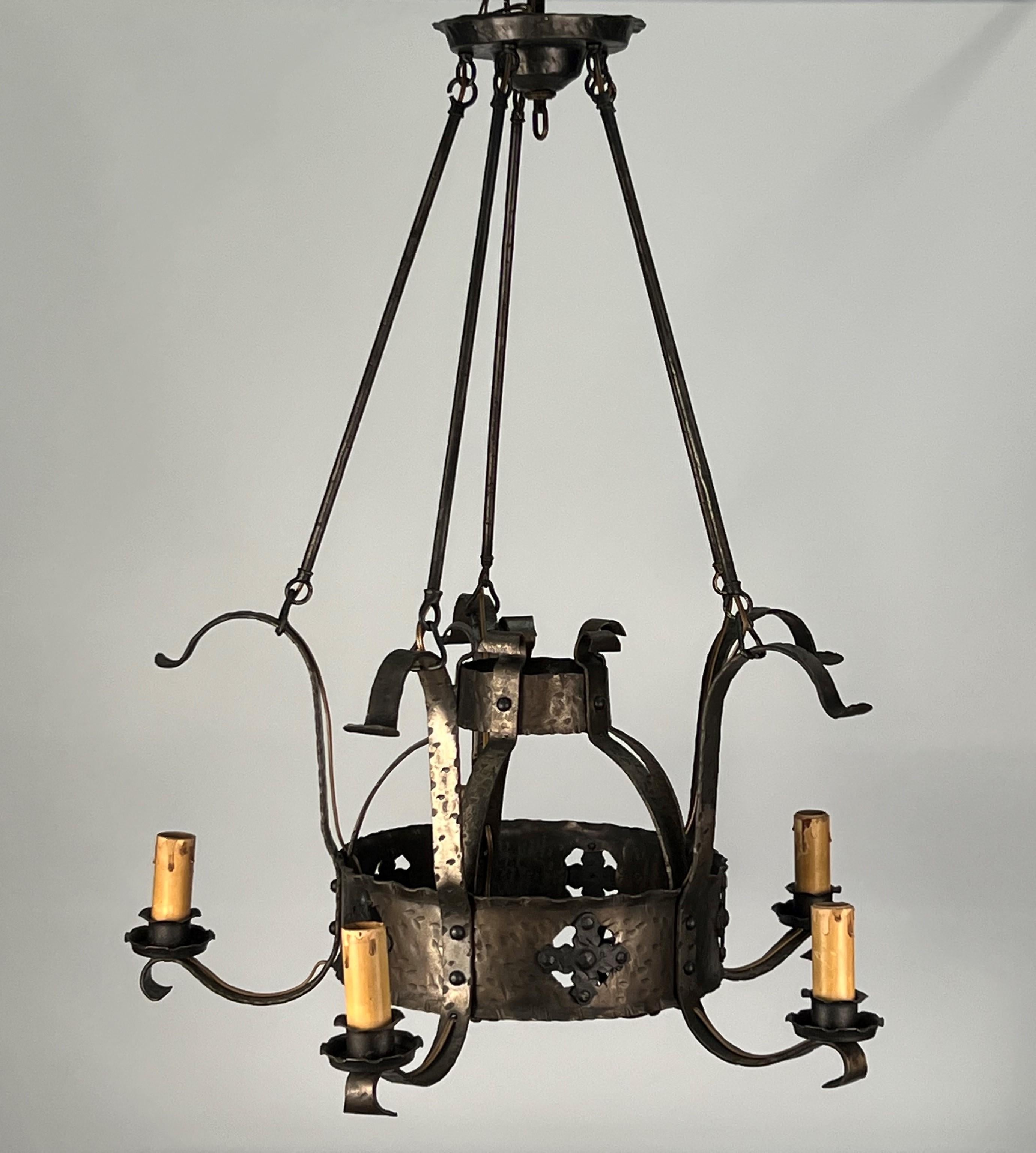 A rustic 1920's American wrought iron chandelier featuring five medium base candle sockets with original drip candle sleeves. Each of the candles are attached to a central steel strap by decorative flat iron curling supports. The interior features a