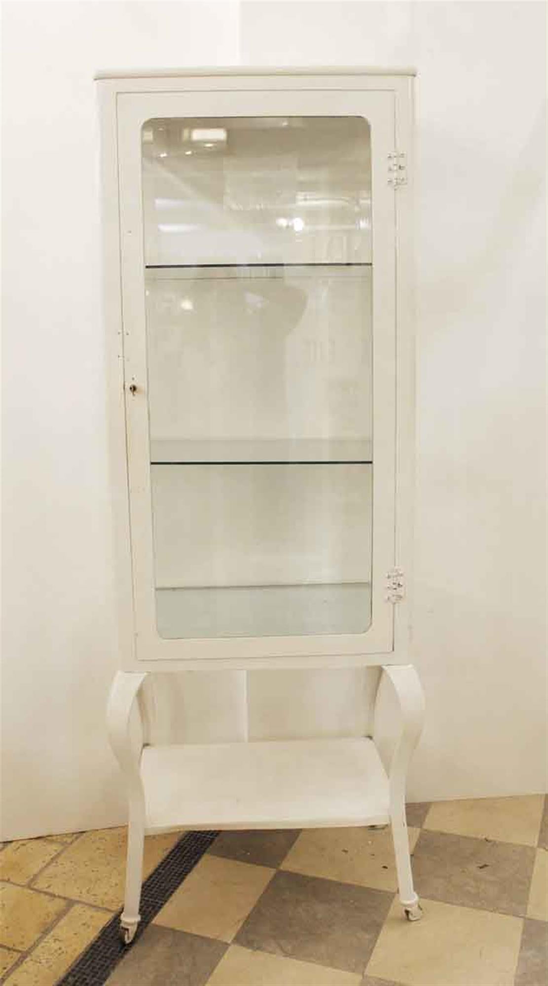 Early 20th century circa 1920 painted white metal medical cabinet with cabriole legs and original beveled glass on the front and sides. This cabinet includes two glass shelves. This cabinet is made from cold-rolled steel and was used in hospital