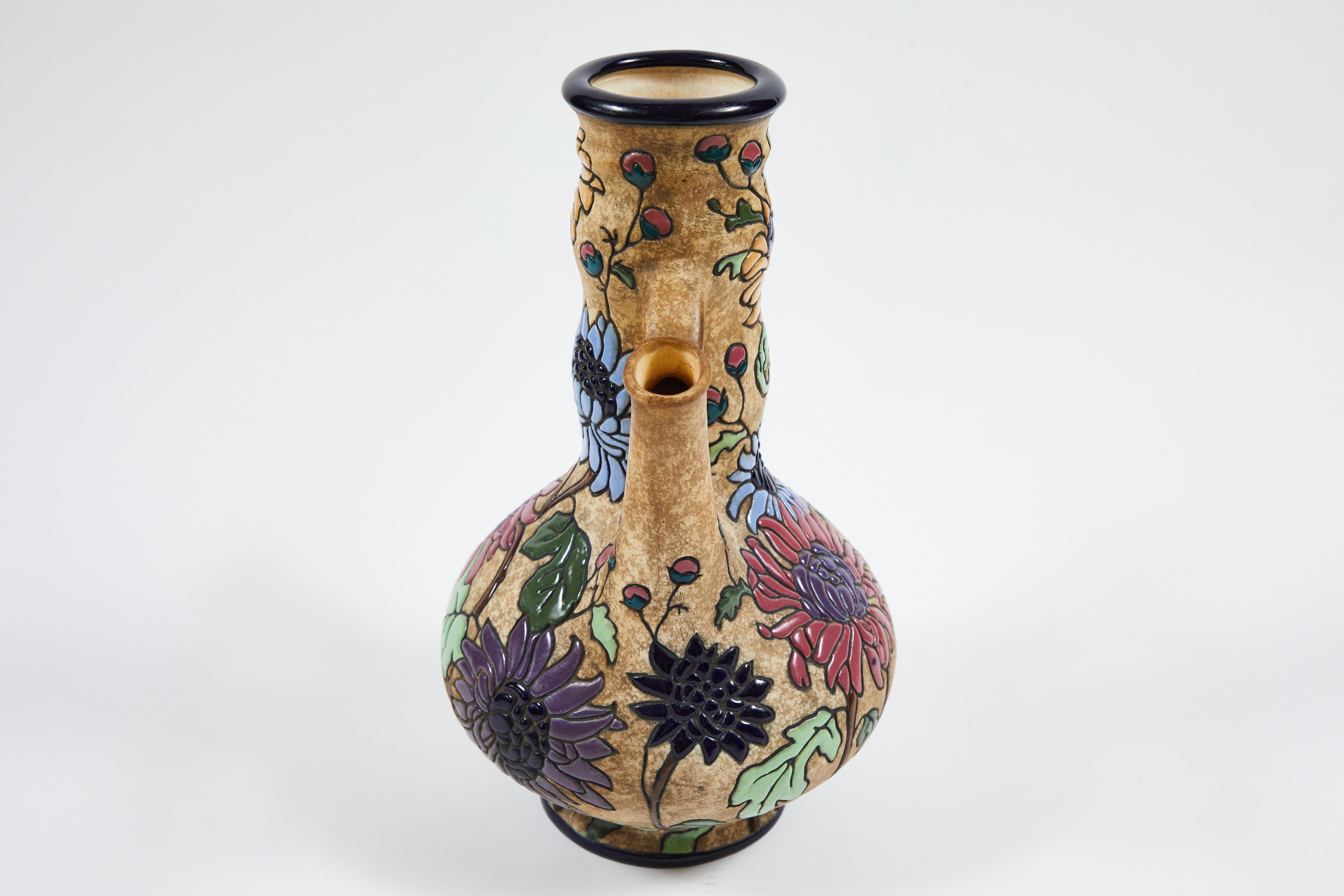 This is a circa 1925 Amphora Campina enameled tall pottery vase with two spouts from Czechoslovakia. The polychrome chrysanthemums are in bright Art Nouveau inspired colors: periwinkle blue, rose pink, Seafoam, marigold, and violet. Stamped on