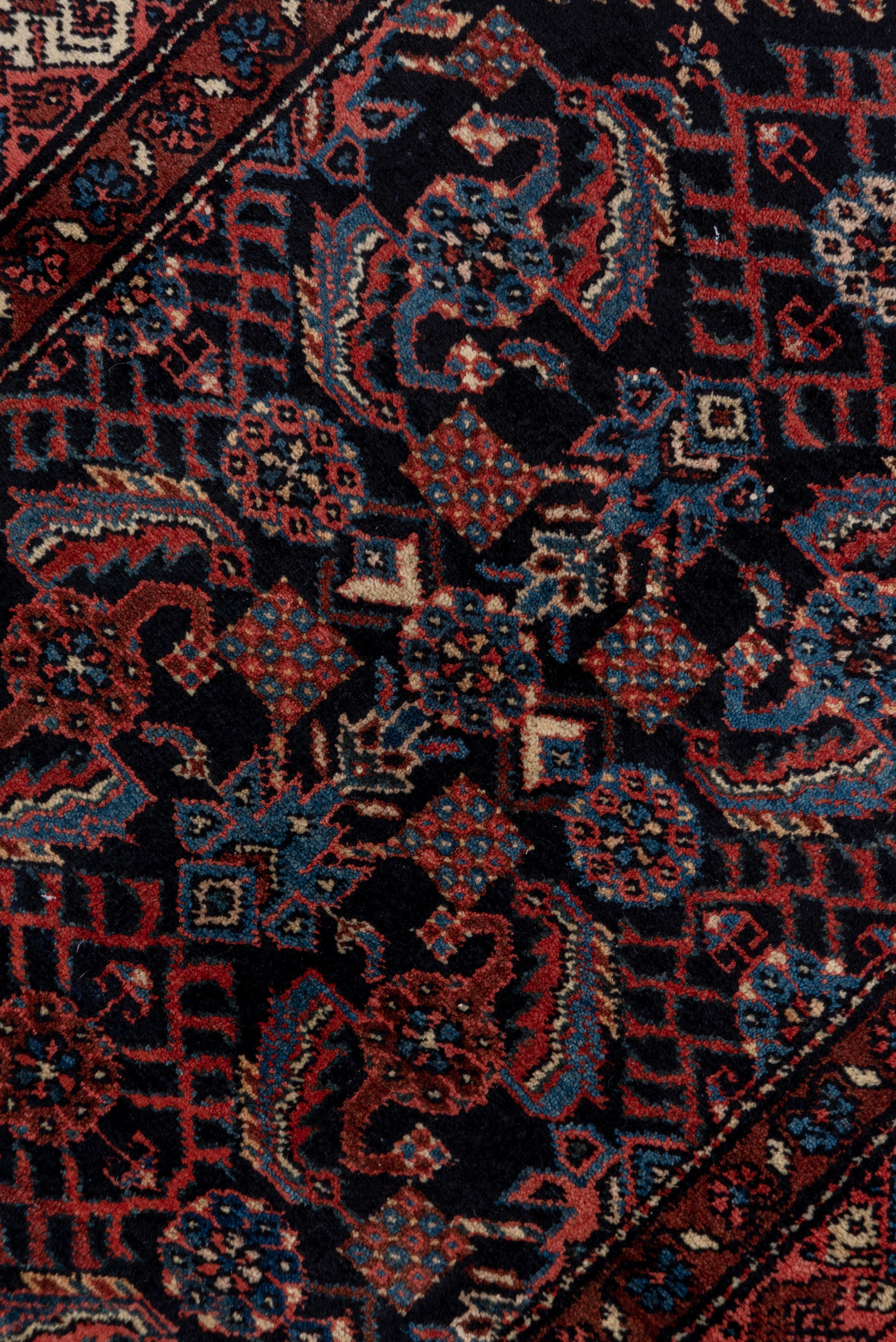 This moderately woven, cotton foundation West Persian rural runner shows a navy ground filled with an extensive all-over Herati design accented in denim blue, coral and ivory. Hook-fringed open central diamonds. Striped triangular corners and