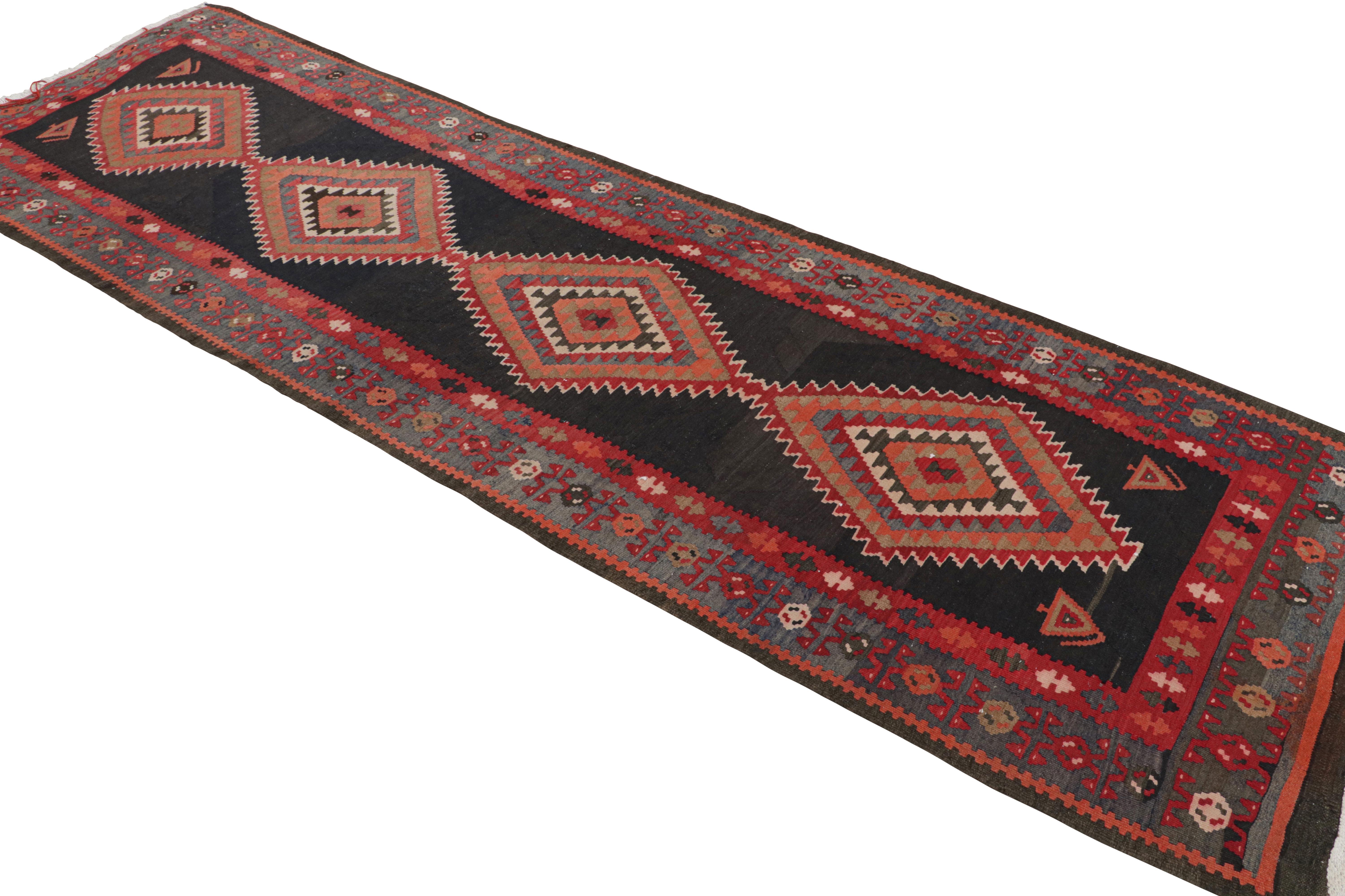 Handwoven in wool circa 1920-1930, this 4x12 antique Perisna Kilim connotes a Kermanshad rug design, exemplifying bold tribal aesthetics of its traditional style. This particular piece sports a rare black background to host a positive-negative