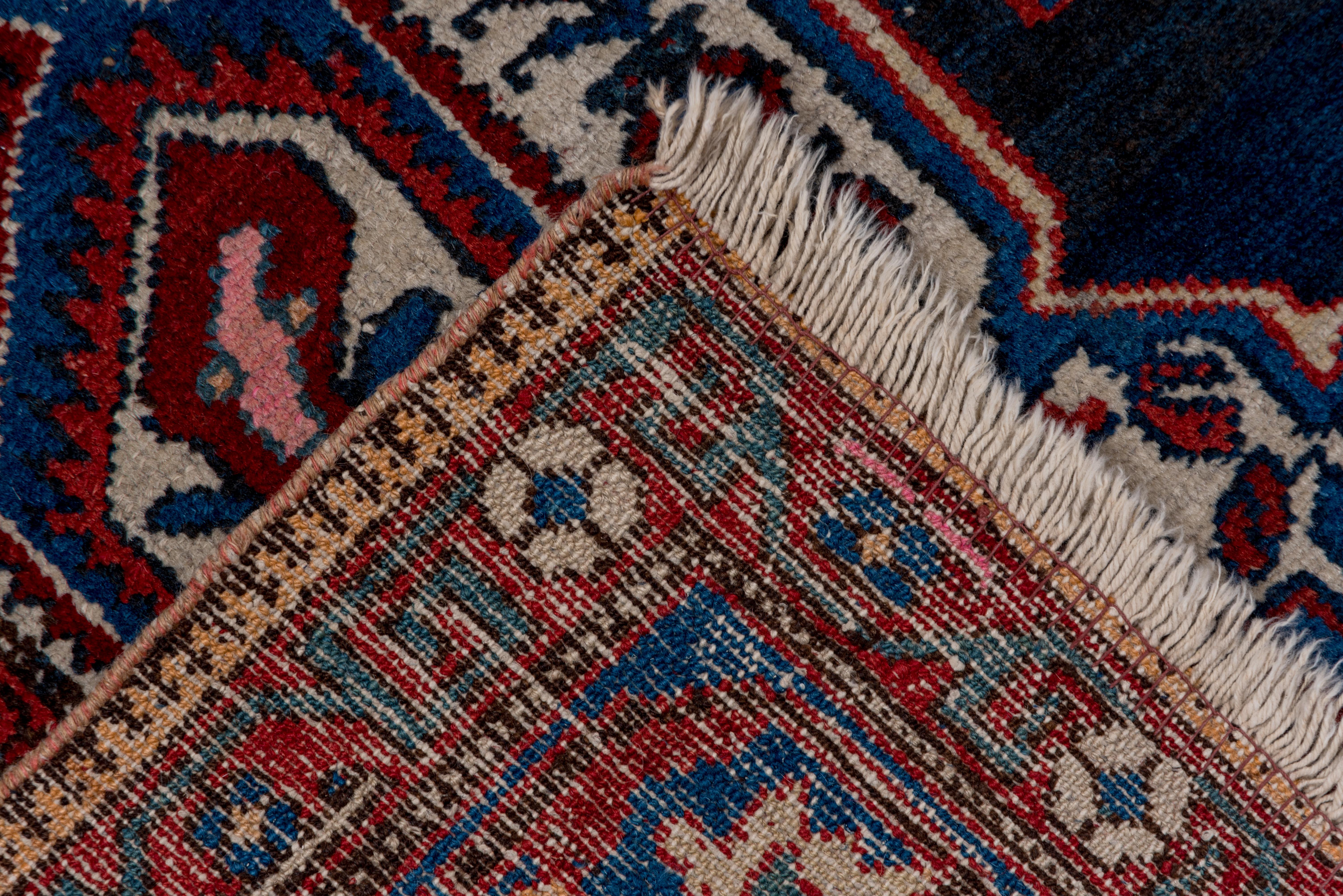 Often attributed to the Char Mahal weaving area, this boldly colored west Persian medallion rug drawn in the angular Heriz style employs a navy ground with a wild pendanted ivory centerpiece with en suite corners, and a medium blue geometric