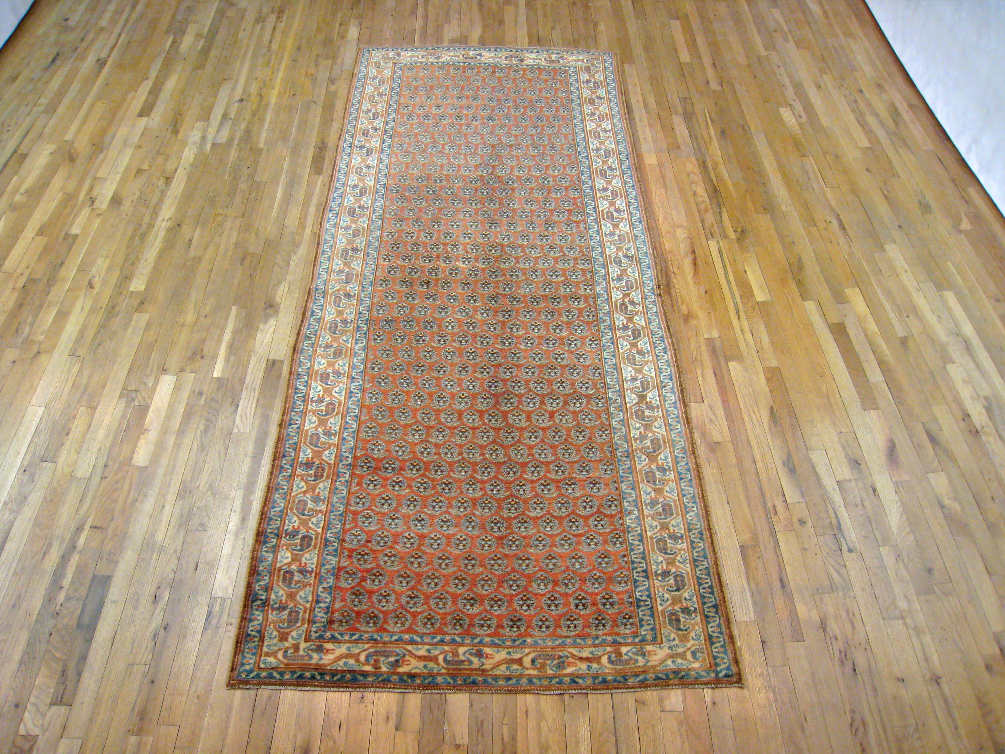 An antique Persian Saraband oriental rug in kaleghi (gallery) size, size 10'7 x 4'3, circa 1920. This lovely hand knotted carpet features a repeating small scale boteh (paisley) design in the soft red central field. The field is enclosed within a
