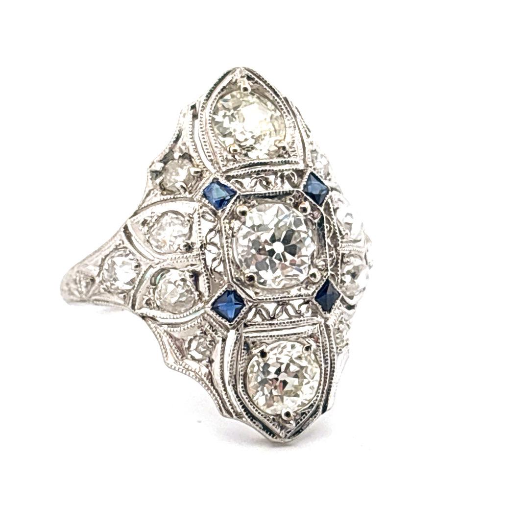 Cette bague est un magnifique exemple de l'art déco des années 1920. La bague en platine présente un design géométrique saisissant, orné de diamants et de saphirs. En son centre se trouve un étincelant diamant de taille ancienne européenne, flanqué