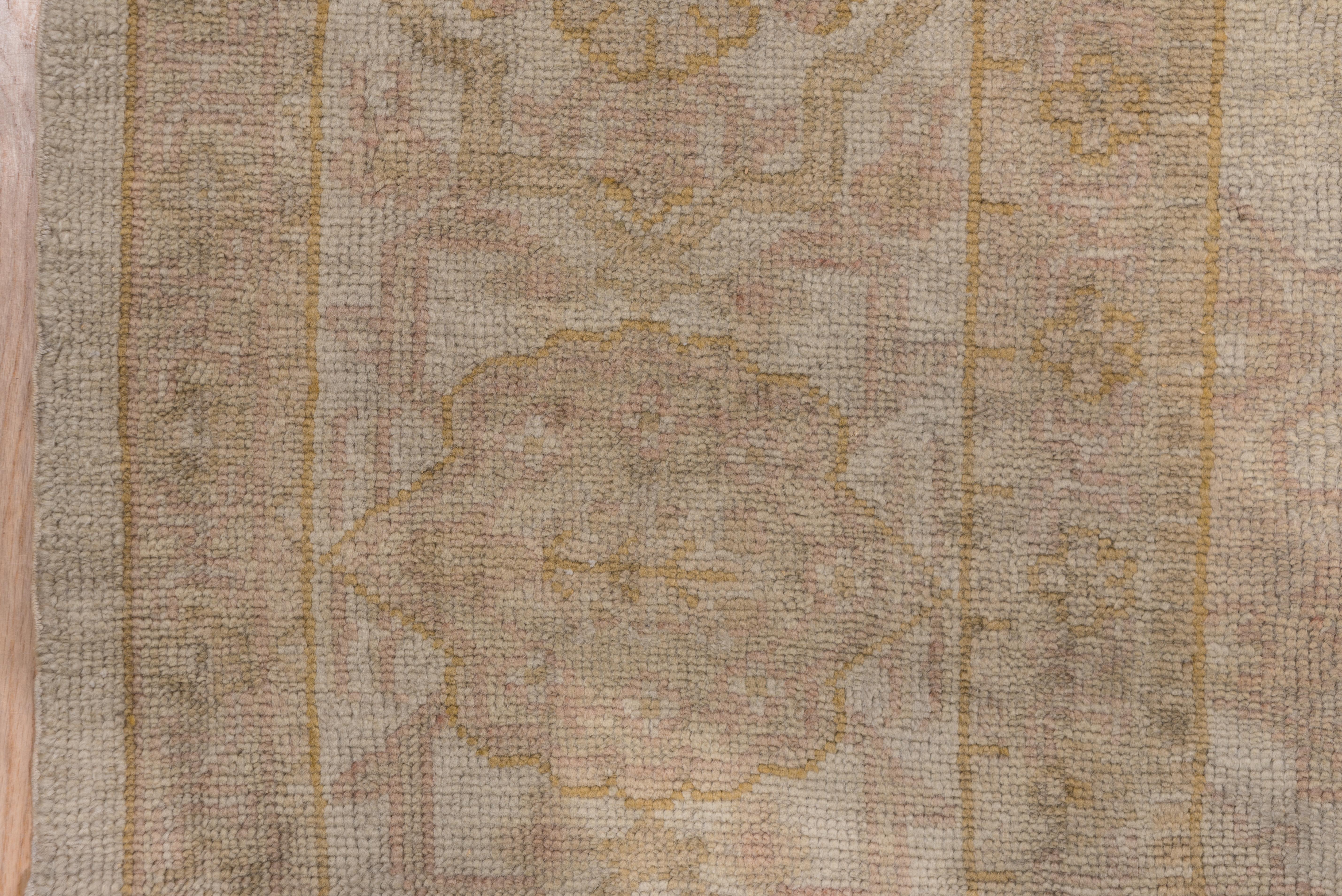The eggshell old ivory field shows small palmettes and thin connecting systems around a central medallion, set off by the ivory main border with details in mustard gold and light pink. Light medallion outlines make this an allover pattern carpet.