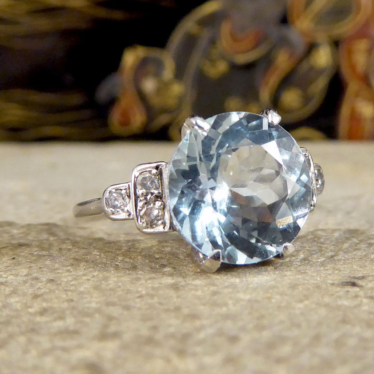 This lovely Art Deco ring features a 2.75ct Round Cut Aquamarine in the centre with a four claw setting. On either shoulder sit a horizontal pyramid of round cut Diamonds, closest to the Aqua are two stones, followed by a single stone closest to the