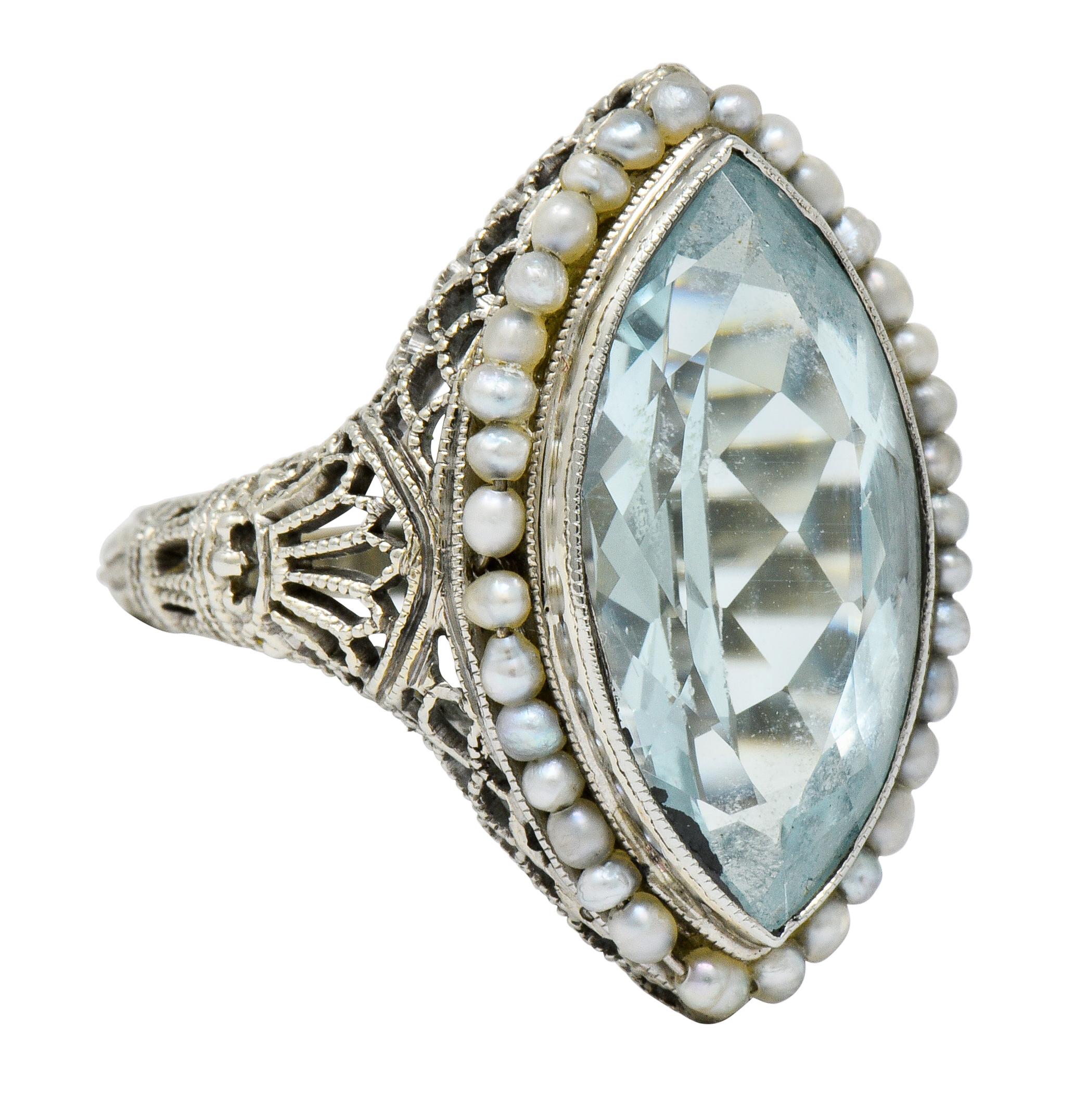 Dinner style ring centering a mixed cut marquise aquamarine, transparent and light blue in color

Bezel set in a navette mount featuring a pierced scalloped gallery and a fully engraved foliate shank

Accented by a surround of strung seed pearls,