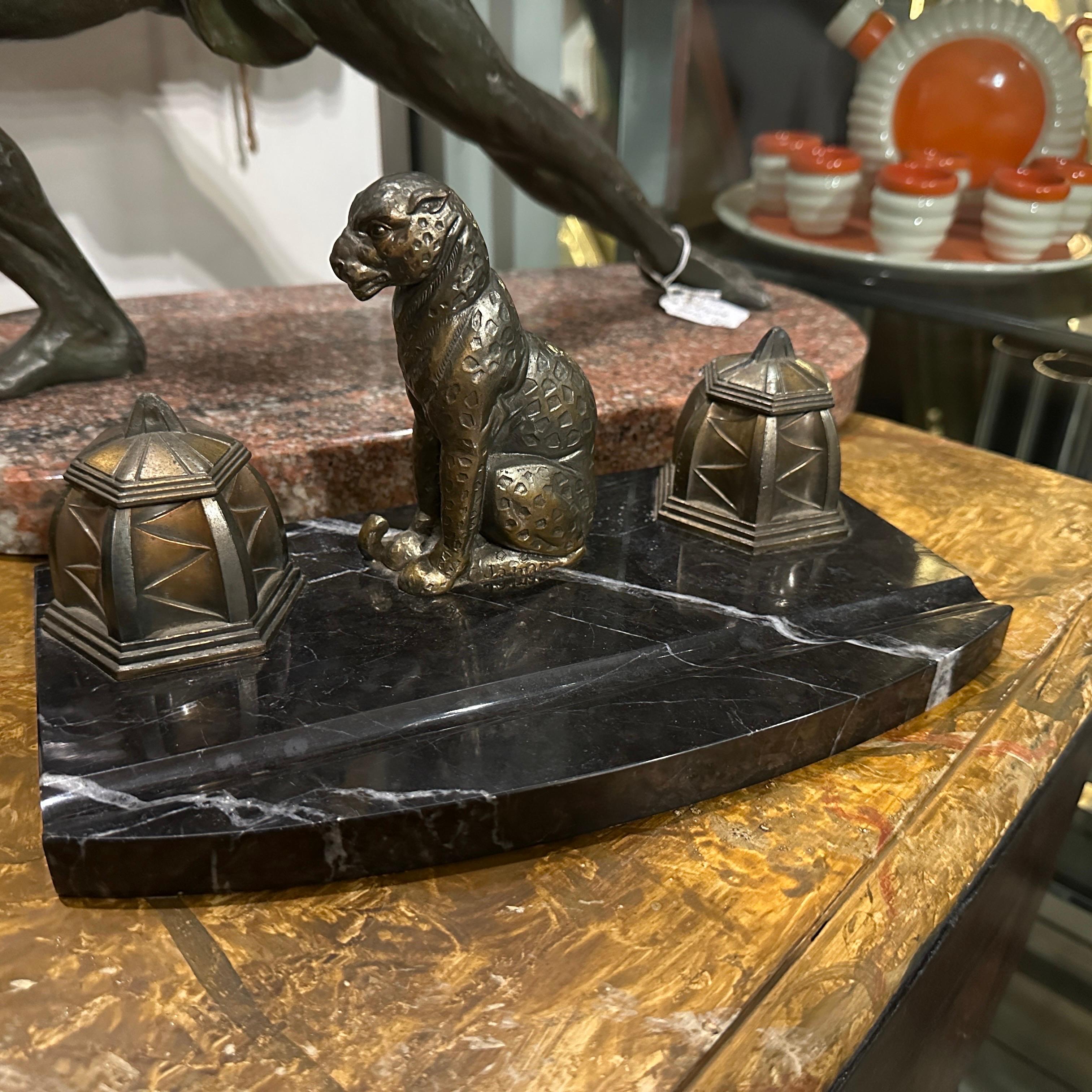 This is a 1920s French Art Deco inkwell made from black and white marble with metal detailing. The centerpiece of the design is a metal sculpture of a leopard, showcasing sleek geometric patterns that typify the Art Deco style. On either side of the