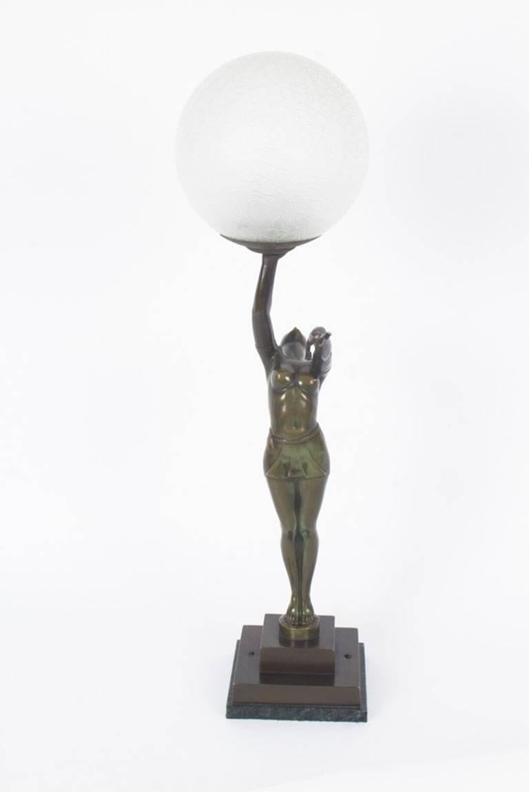 This is a beautiful antique Art Deco bronze lamp depicting a dancing maiden, circa 1920 in date.
 
This lamp depicts the excellently patinated bronze figure of a semi-naked maiden in a gracious dancing pose holding a glass sphere lamp over her