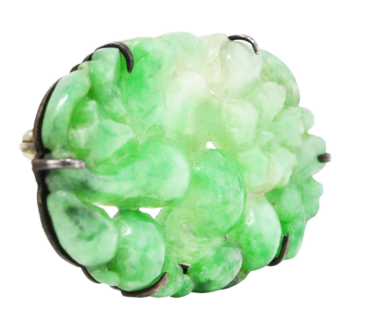 East to West oval brooch is comprised of intricately carved jadeite jade. Depicting scrolling and highly rendered foliate, fruit, and flowers. Translucent and moderately mottled green to very light pastel green. Talon set and mounted on a sterling