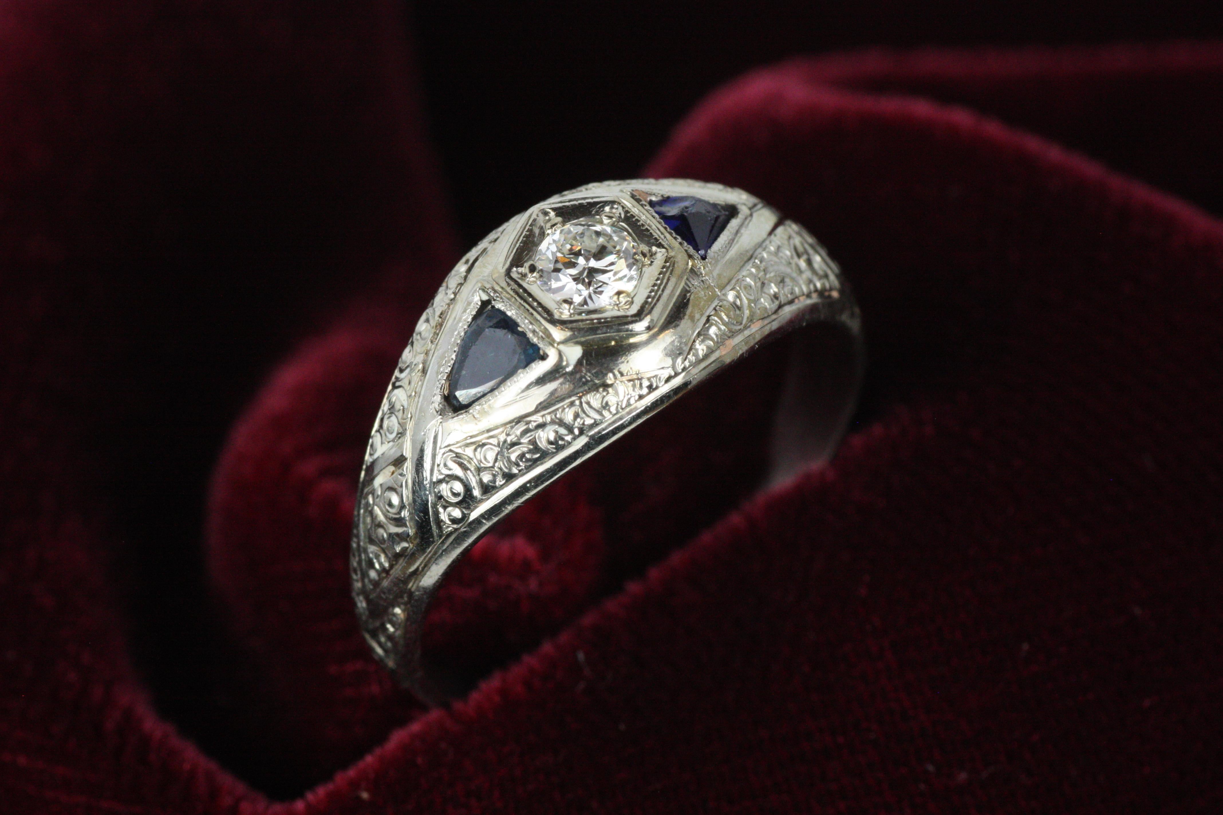 Art Deco dome style ring from our antique fine jewelry collection at Bracken Jewelers. It is from the 1920s and features a 0.16 carat round brilliant cut diamond, flanked by two triangular blue sapphires – one natural and on synthetic (chipped).