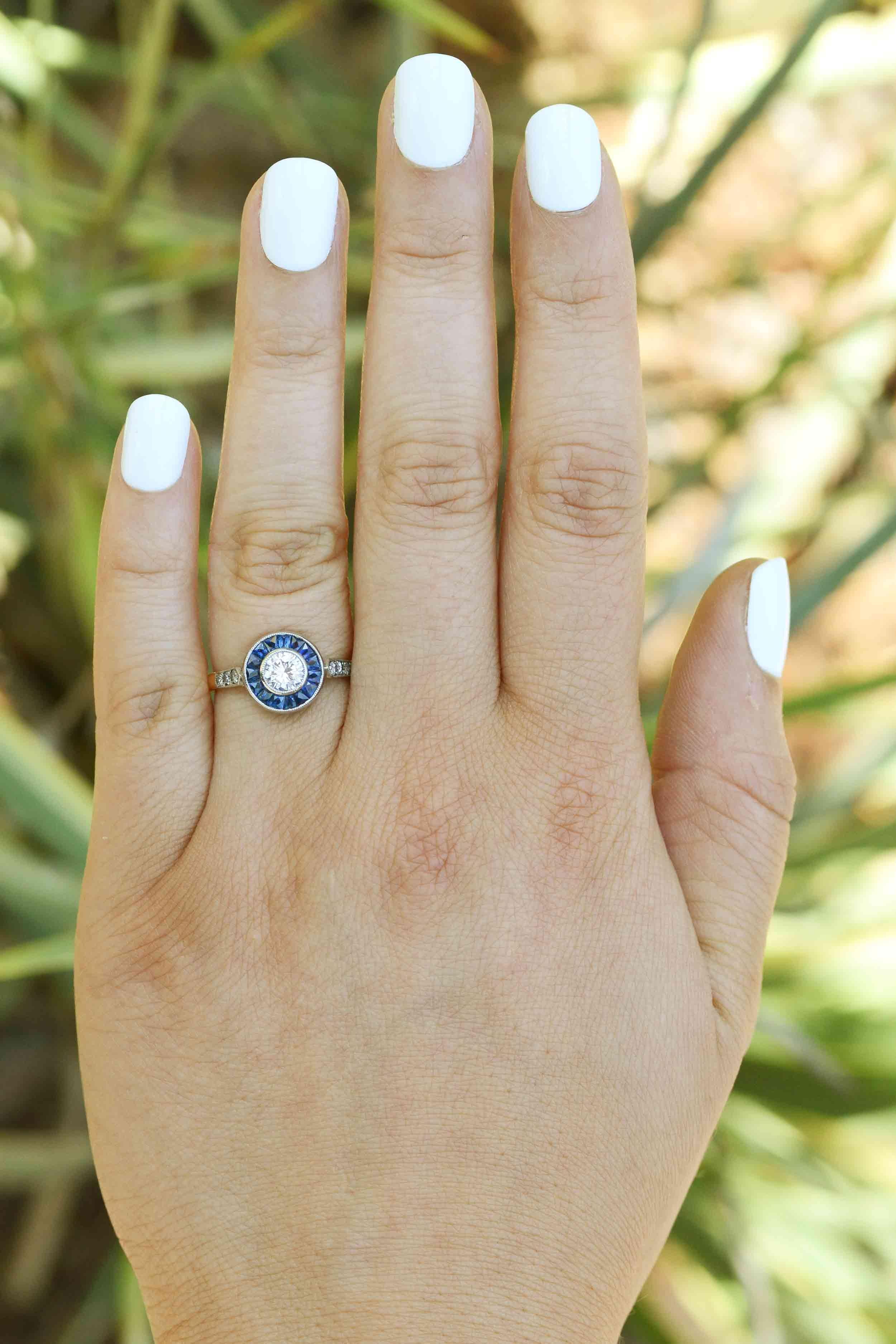The Brentwood is an enchanting 1920's Art Deco diamond and sapphire target engagement ring centered by a lively, fiery 1/2 carat round diamond. The halo of velvety-blue calibre' cut sapphires embraced by a milgrain-kissed low bezel setting makes it