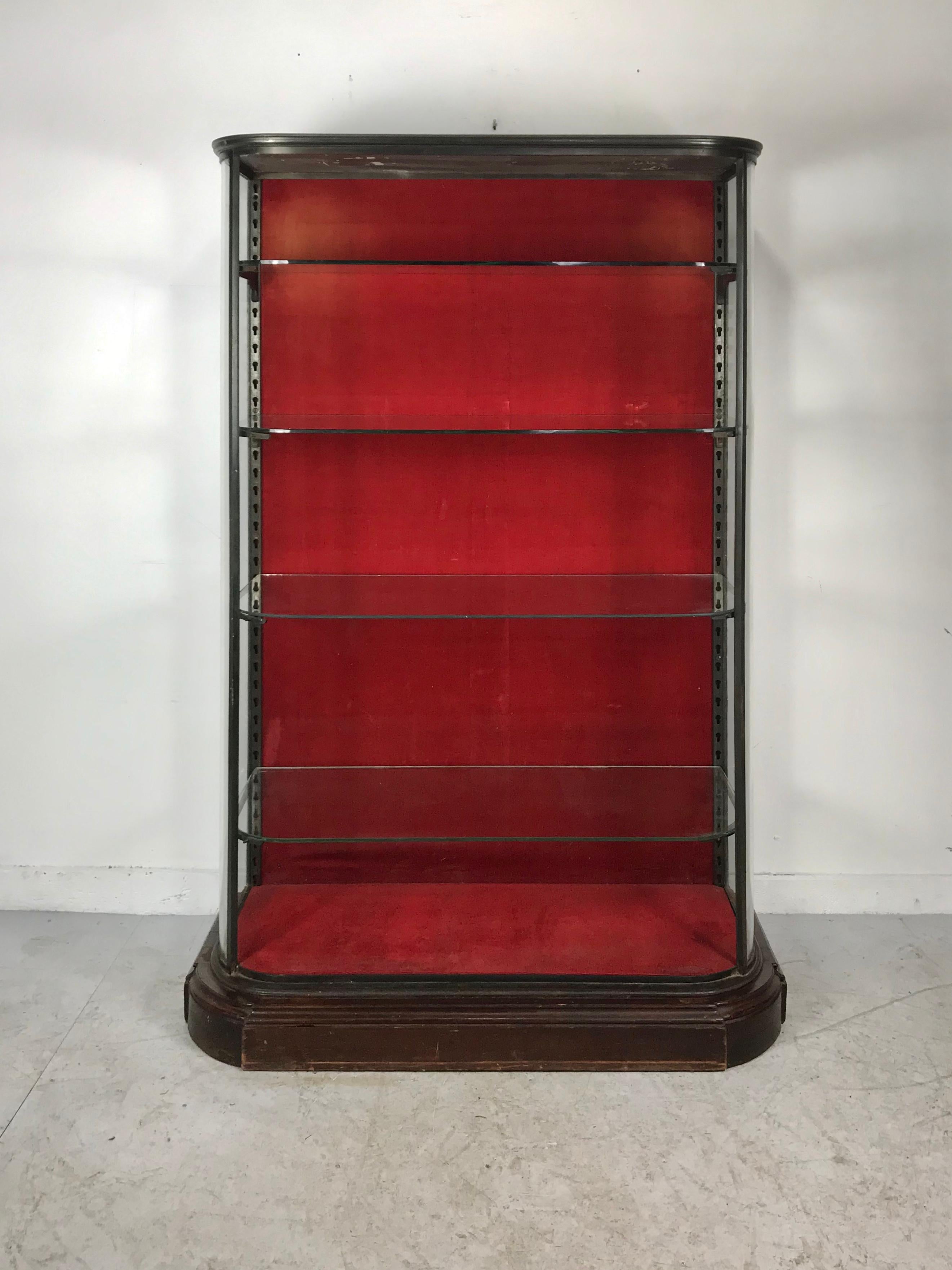 Stunning, simple and elegant vitrine, store display, cabinet. Possibly French? Four adjustable curved glass shelves, stylized brackets, retains original red velvet back, amazing quality and construction, stylized stepped mahogany wood base, hand